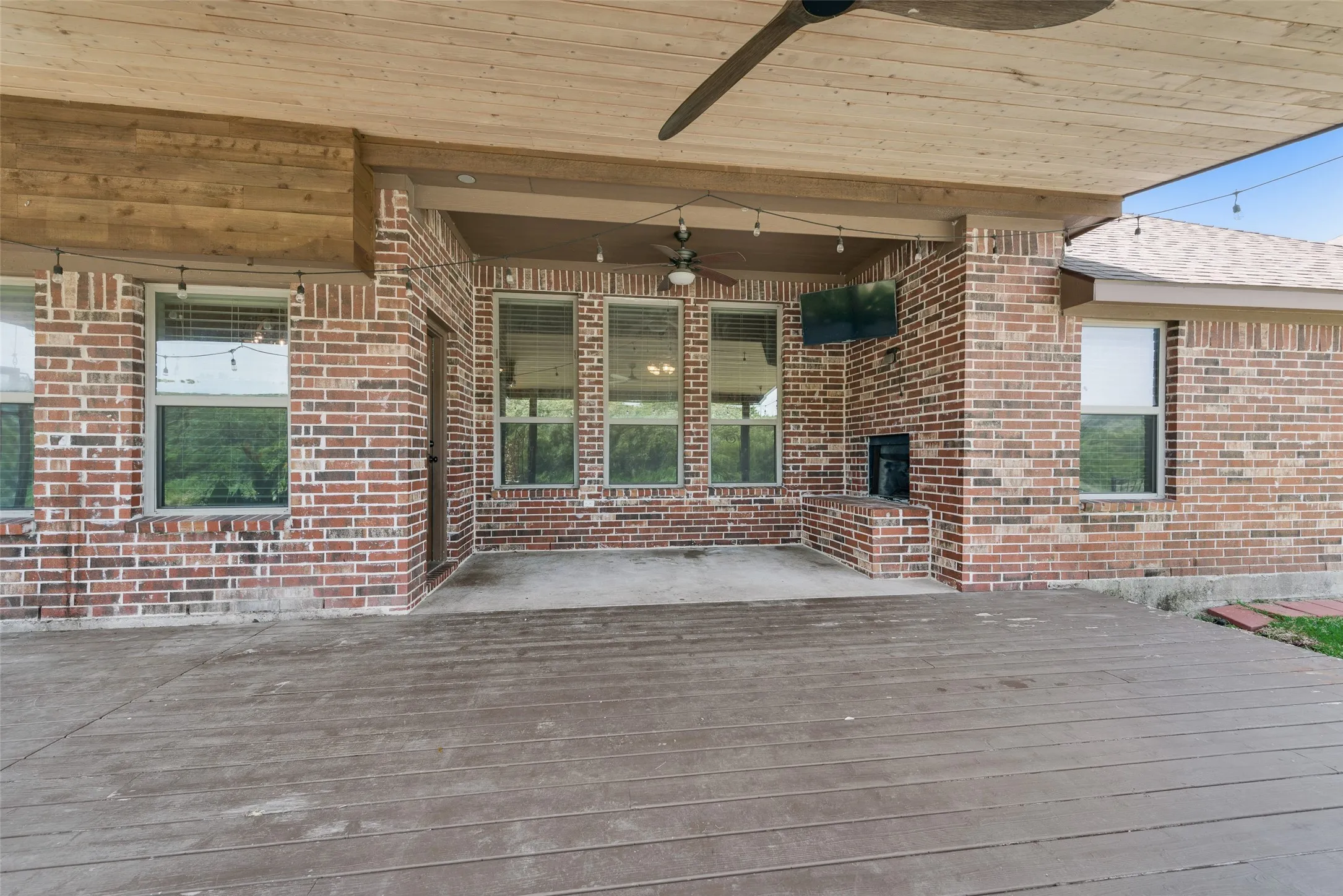 Covered patio with a wood-finish ceiling, brick exterior, ceiling fan, and string lighting