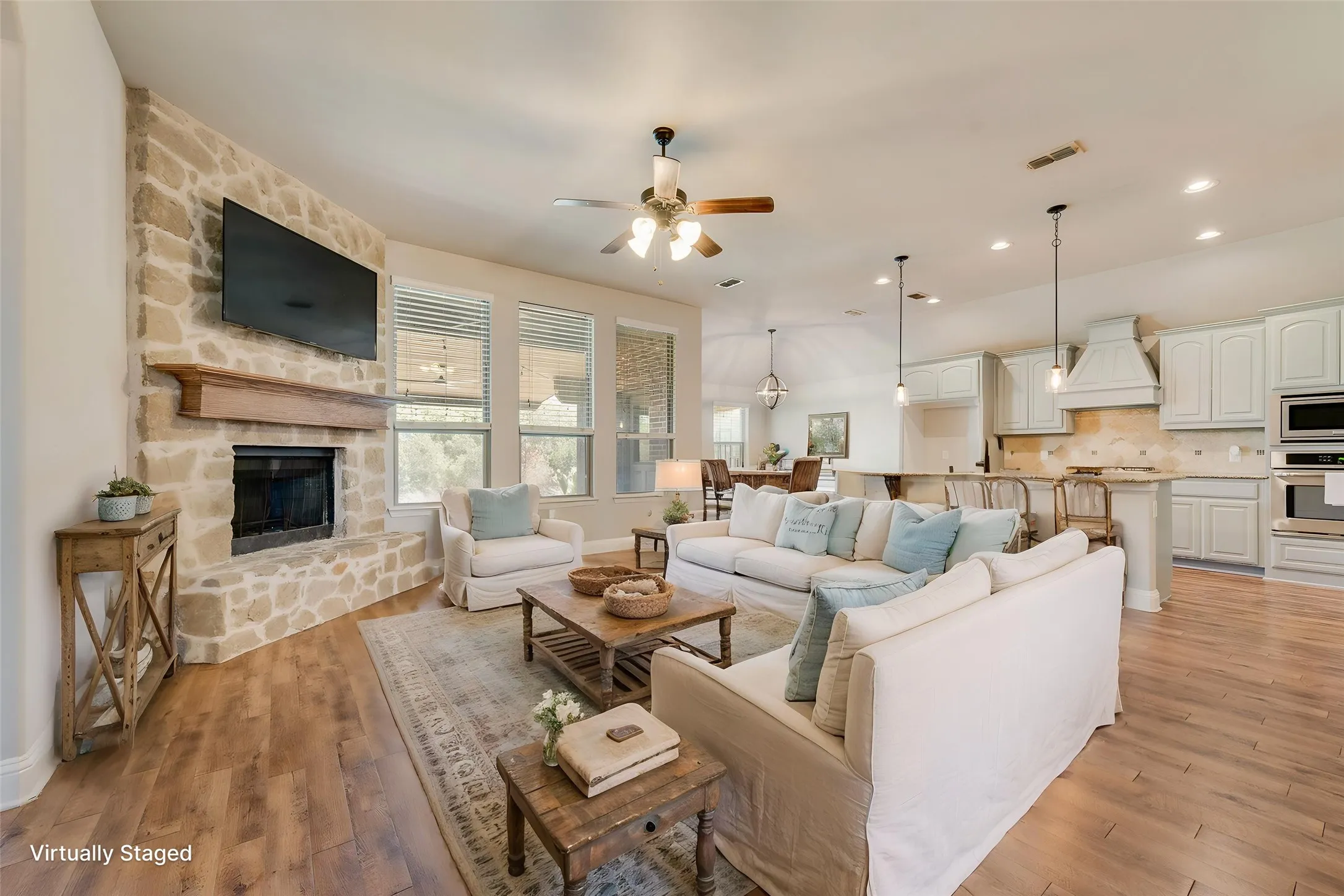 Virtually staged. Spacious room featuring wood-finish flooring, a stone-clad fireplace with a wood mantel, multiple windows, recessed lighting, and a ceiling fan