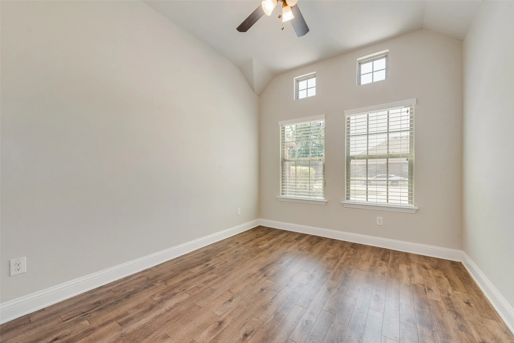 Bright and spacious room featuring soaring vaulted ceilings, a ceiling fan with integrated lighting, and abundant natural light from multiple windows with plantation shutters