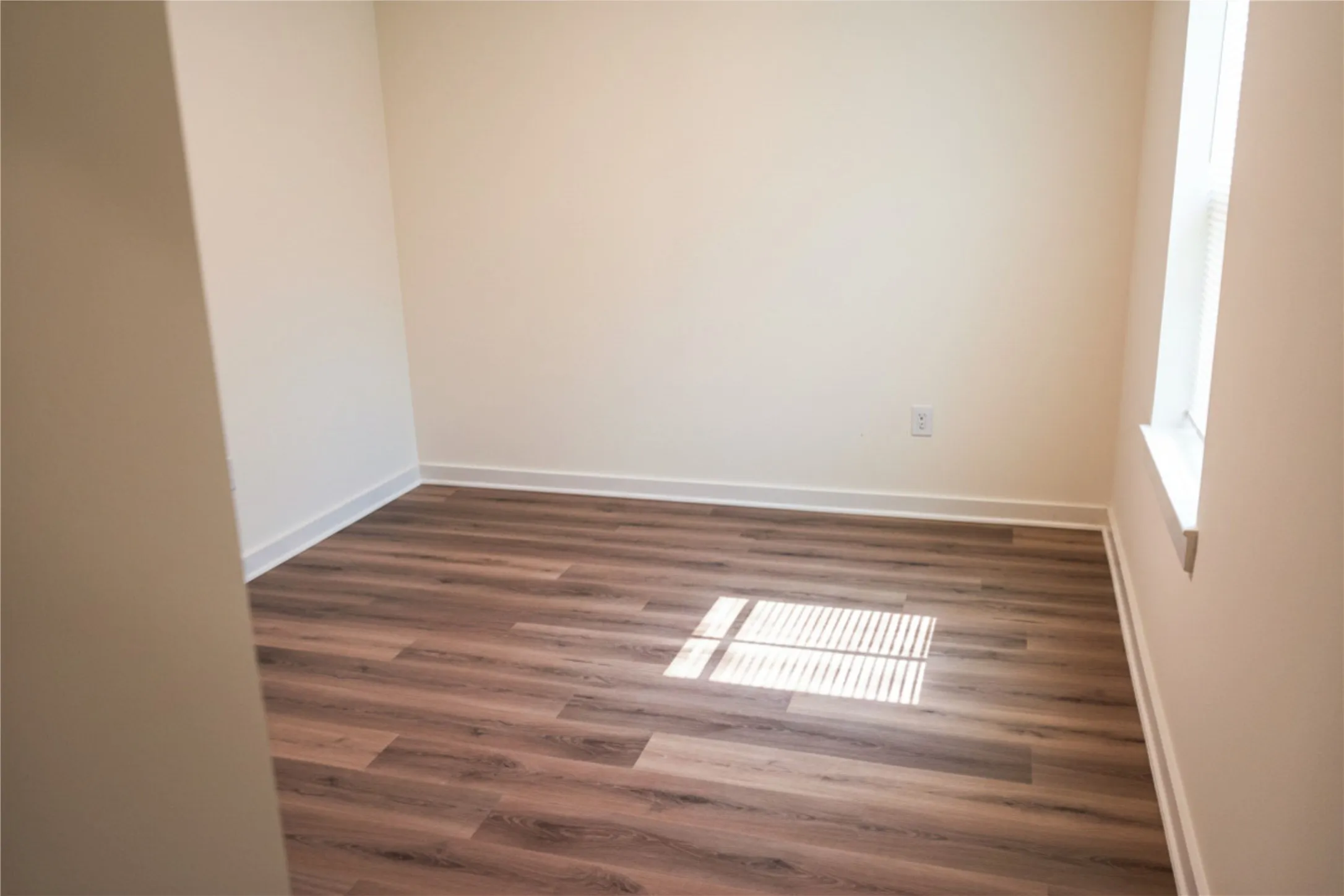 Wood-finish flooring with white trim and a single window
