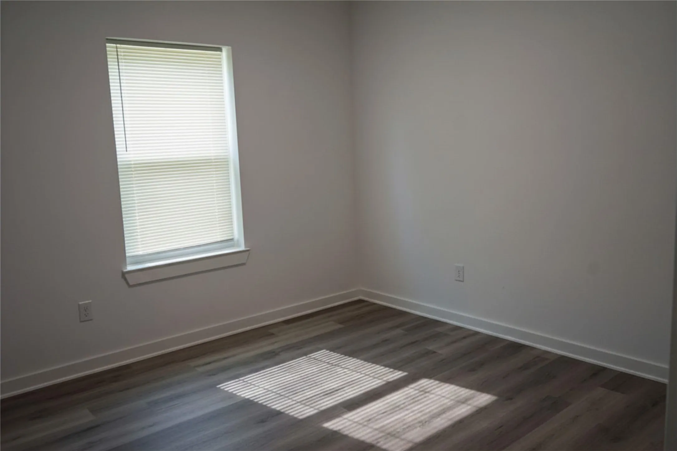 Wood-finish flooring, white walls, and a window with blinds