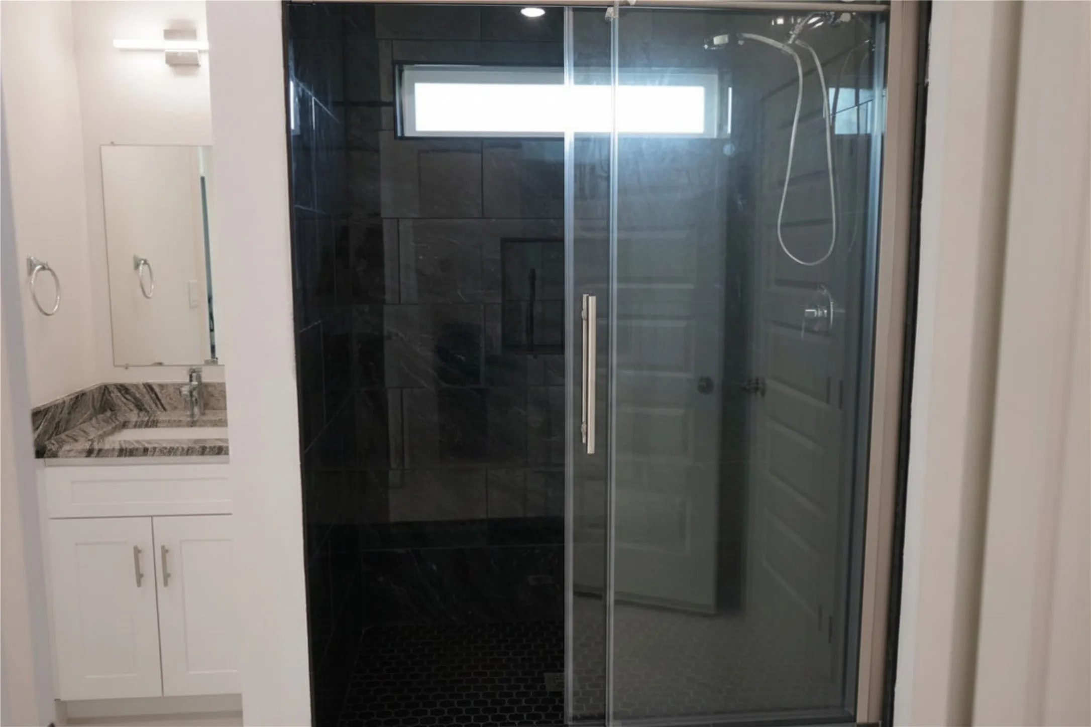 Sliding glass shower enclosure with dark large-format tile walls and a hexagonal tile floor