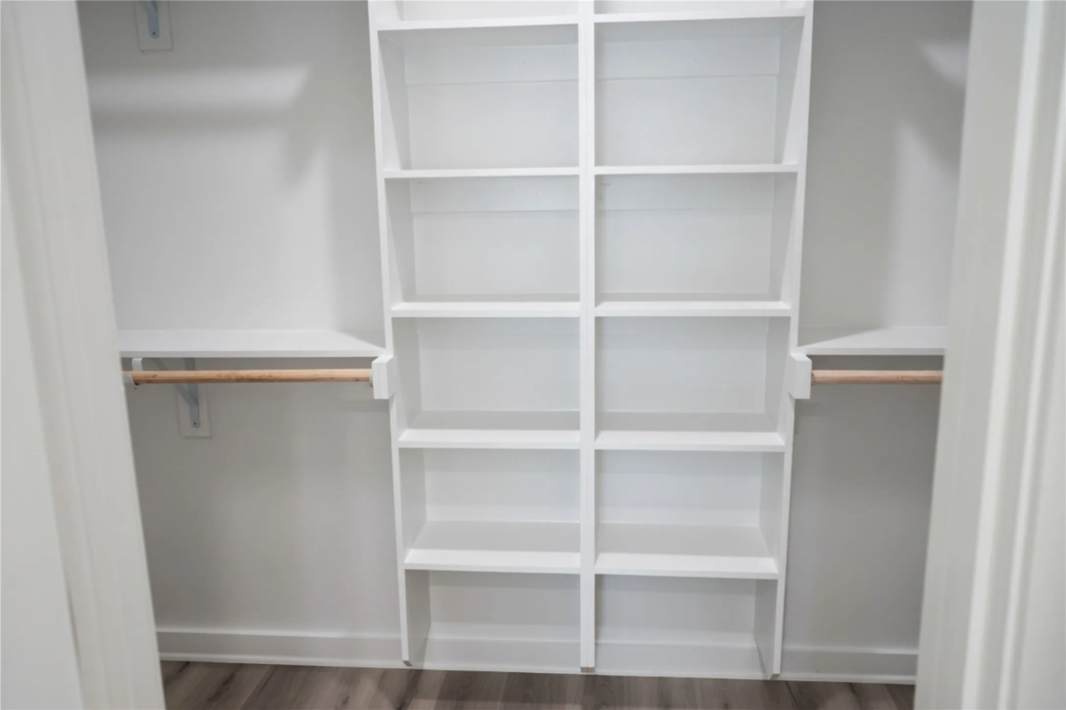 White built-in shelving, white wall shelving, wood-finish flooring, and hanging rods