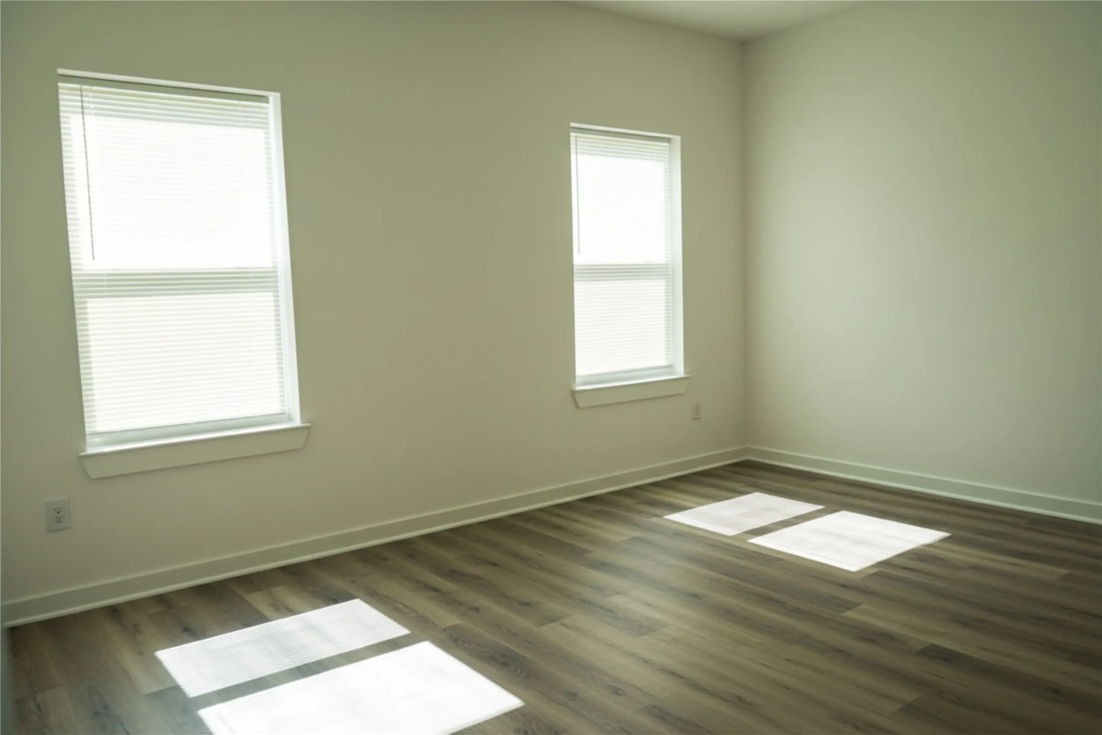 Light-filled interior featuring two windows with horizontal blinds, wood-finish flooring, and crisp white walls