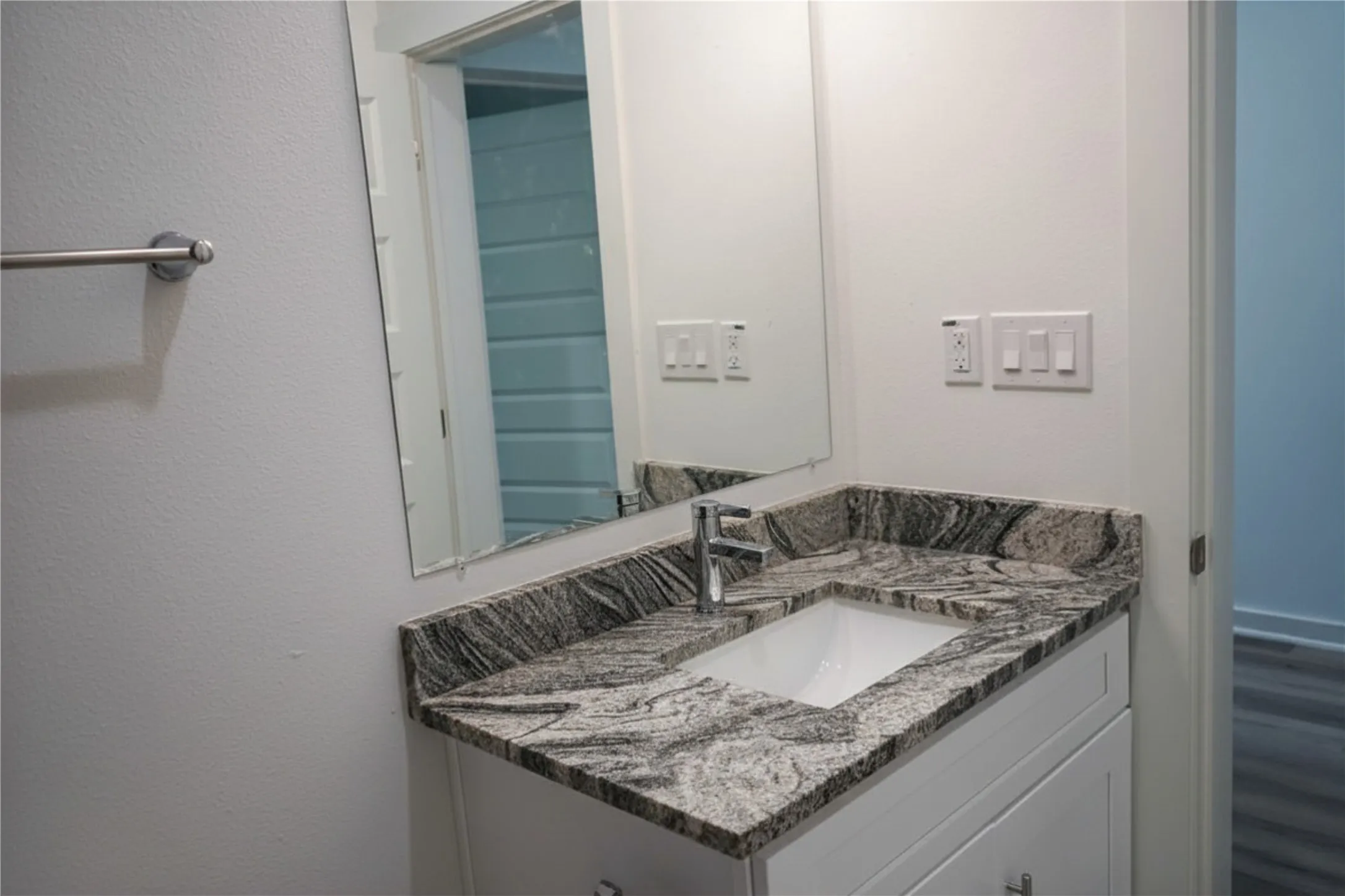 White vanity with a polished chrome faucet, under-mount sink, and granite countertop