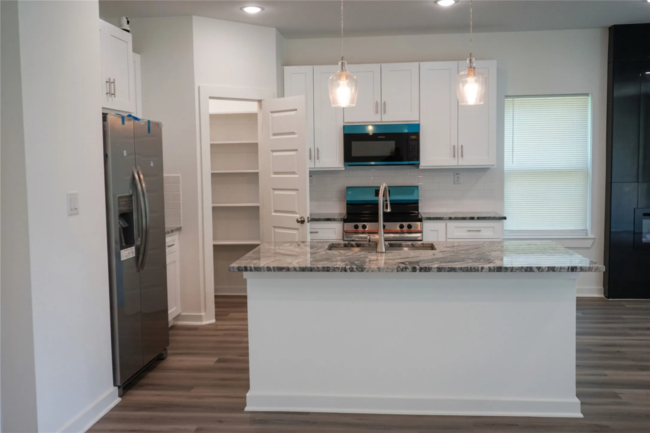 Kitchen featuring white cabinetry, a central island with a stone countertop, stainless steel appliances, and wood-finish flooring
