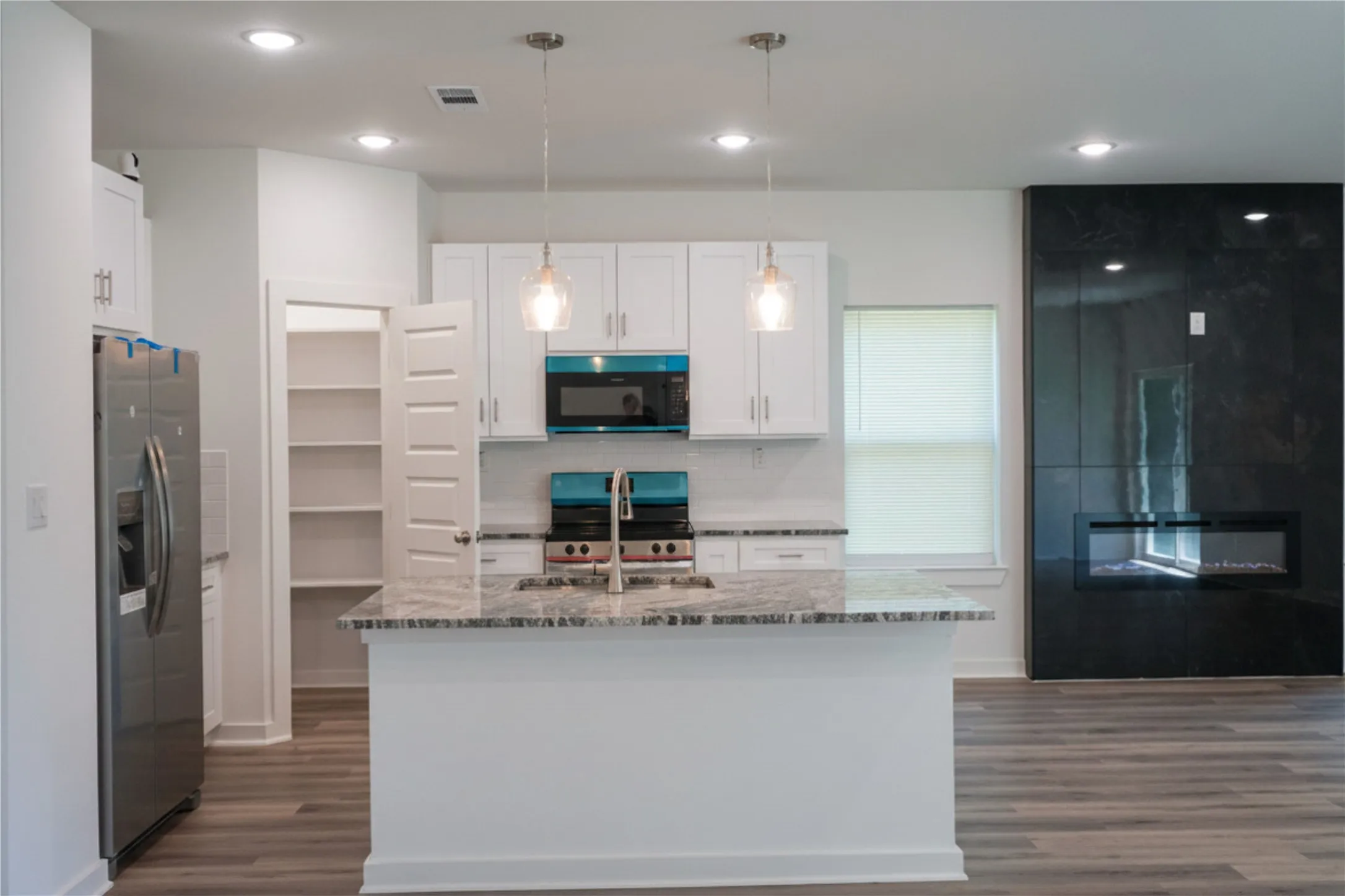 Modern kitchen featuring white cabinetry, a central island with a granite-style countertop, stainless steel appliances, and wood-finish flooring
