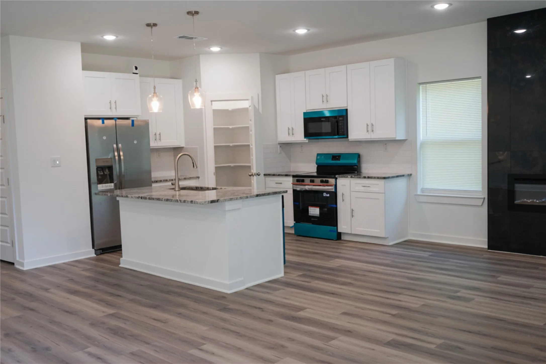 Open-concept kitchen with wood-finish flooring, white cabinetry, a kitchen island with stone countertop, and built-in stainless steel appliances