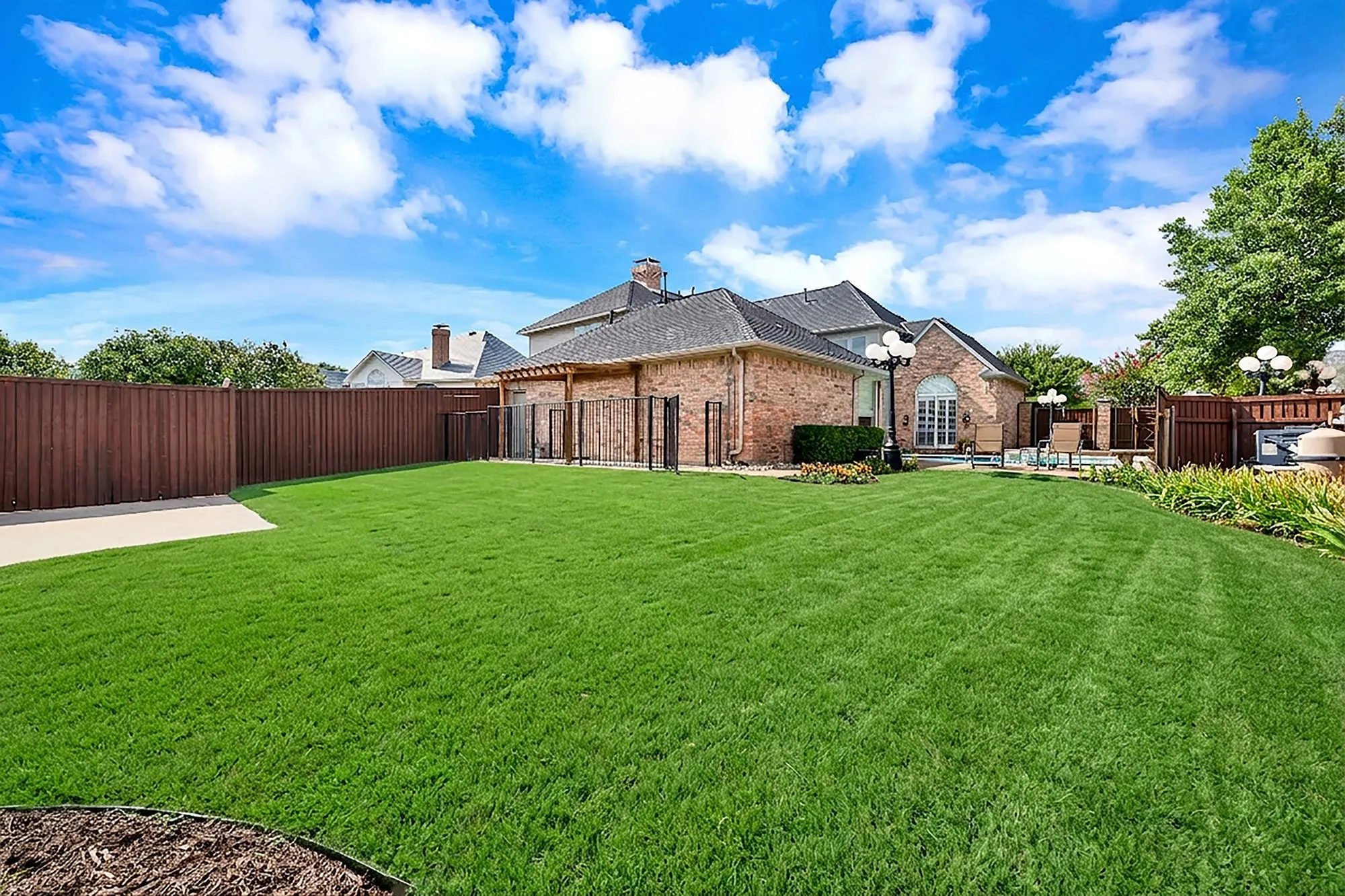 A tall privacy fence encloses an expansive grassy yard bordered by low-maintenance stone paths and safety fencing. Throw a frisbee with the dog or watch kids run freely across lush green grass during weekend family atherings.