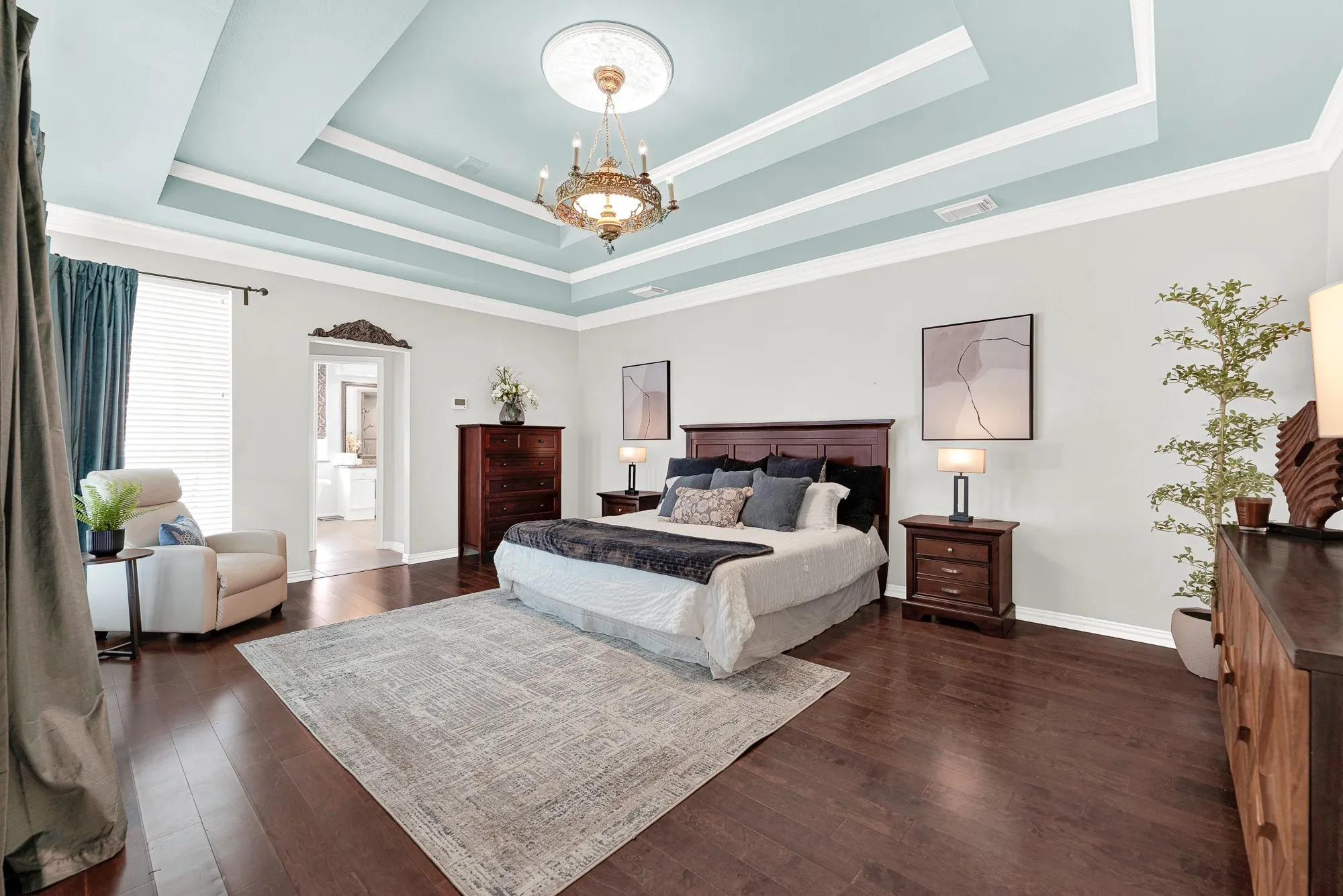 A double-tiered tray ceiling painted soft powder blue draws eyes upward toward a delicate central chandelier. You can wake up gradually under the gentle glow of the soft ceiling light each morning.