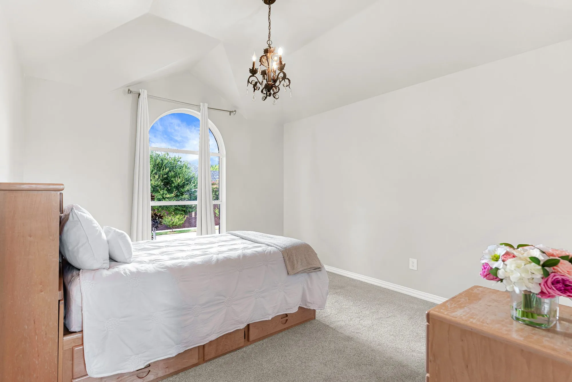 A delicate multi-bulb chandelier hangs from a steep vaulted ceiling directly above a sunlit window arch. Children will love drifting off to sleep under the magical glow of their own glowing light fixture.