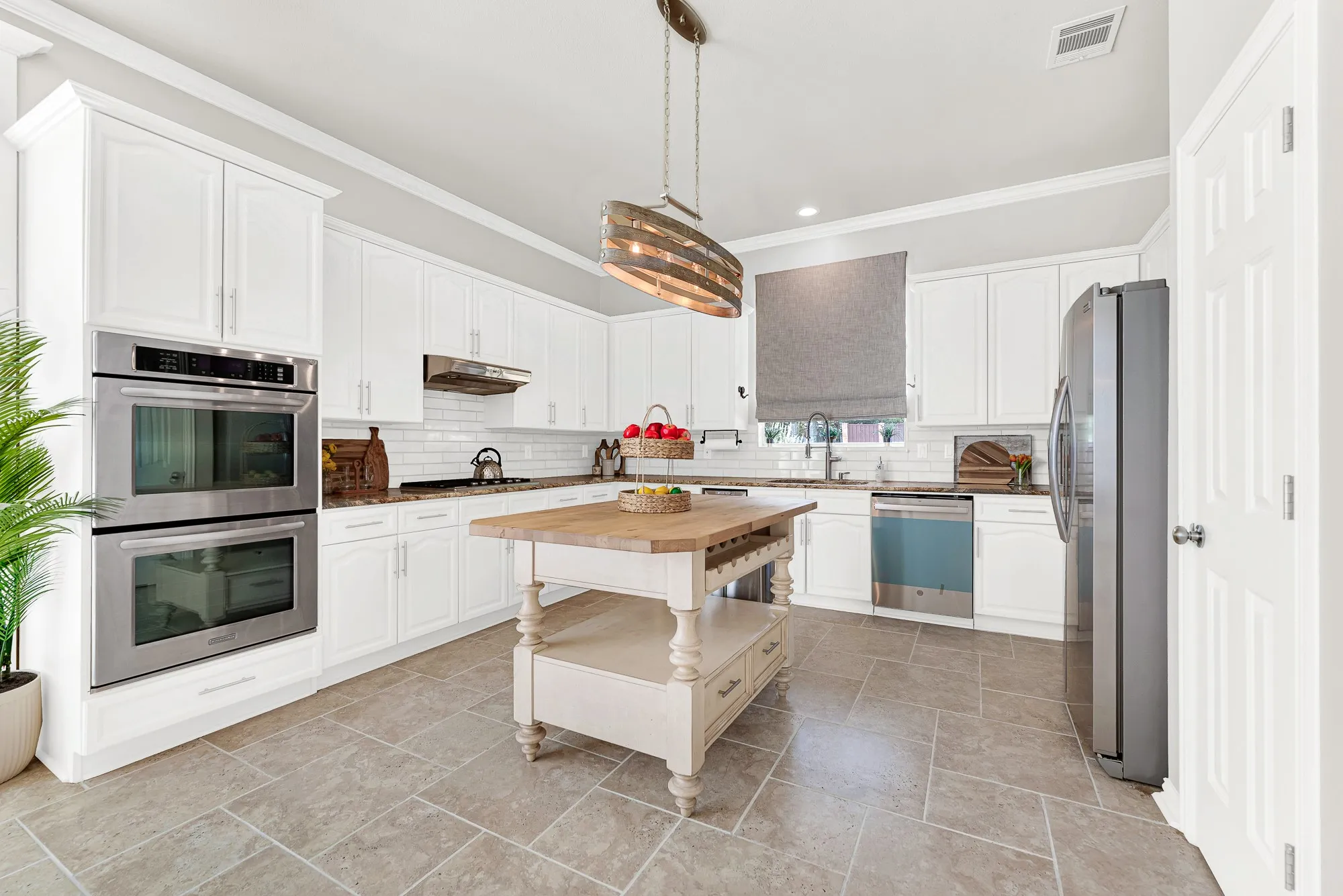 White cabinetry wraps around a central prep island, anchored beneath a rustic oval chandelier hanging from bright, high ceilings. You can bake weekend treats with the kids while delicious aromas fill the airy room