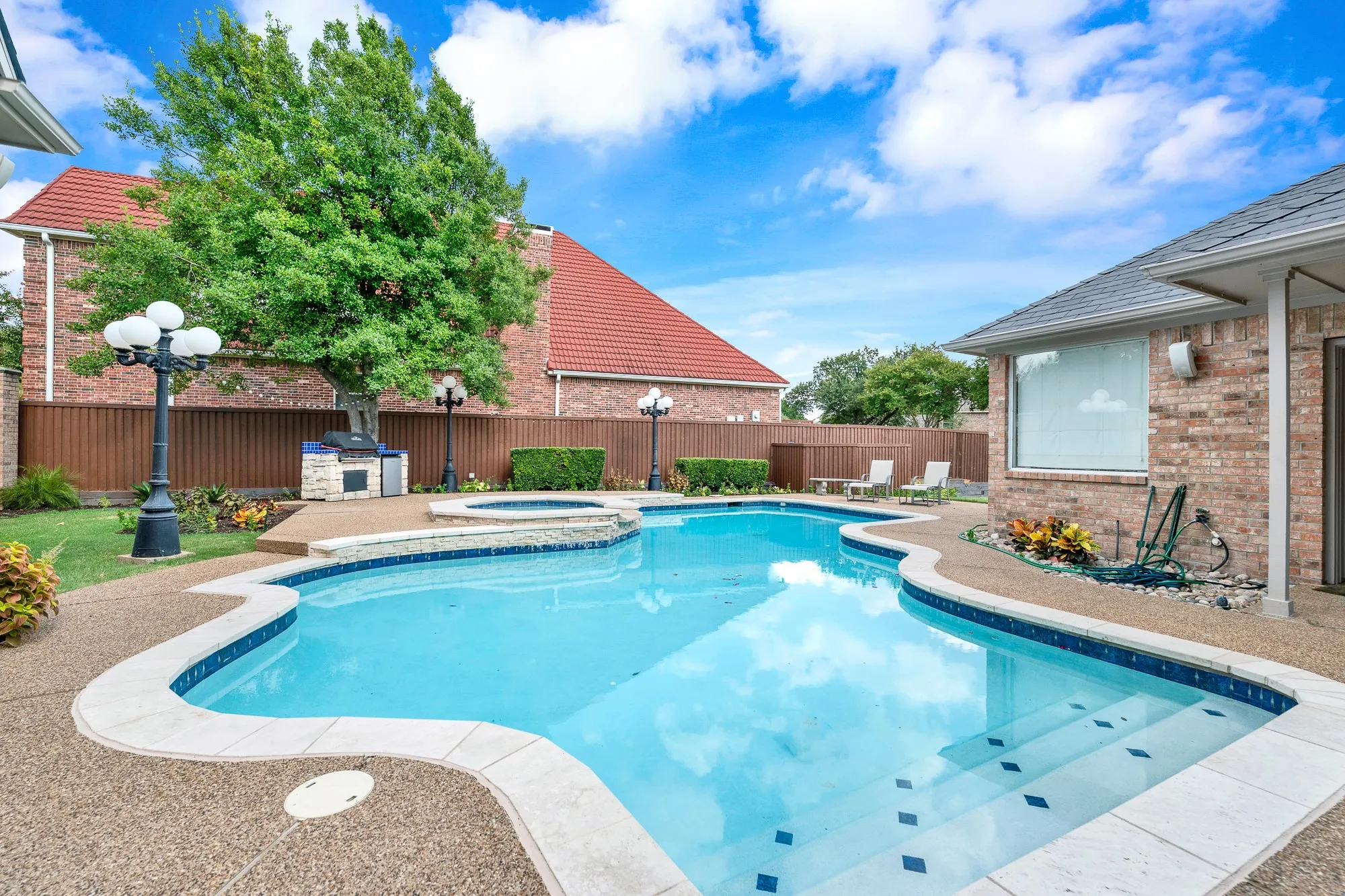 Submerged entry steps lead into clear turquoise water anchored by a built-in stone grilling station along the perimeter fence. Cool off with a refreshing afternoon swim before grilling dinner outdoor.