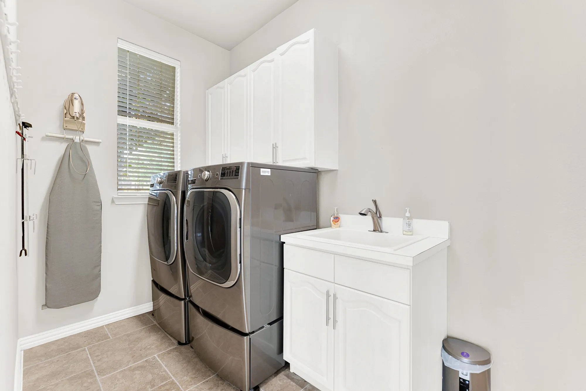 A tall bright window fills crisp white upper cabinetry and a dedicated wash basin with energizing natural light. Effortlessly breeze through laundry day organized inside a clean, light-filled space designed for practical convenience.