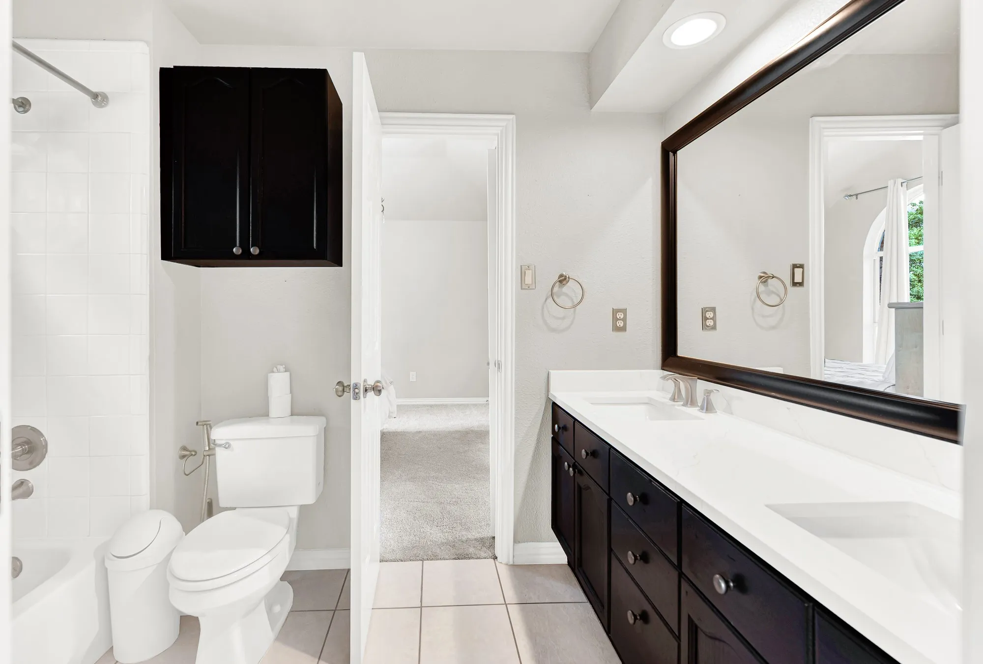 Dark espresso cabinetry provides striking contrast against clean white counters and matching shower tile. Family members can easily freshen up with plenty of personal storage space for toiletries