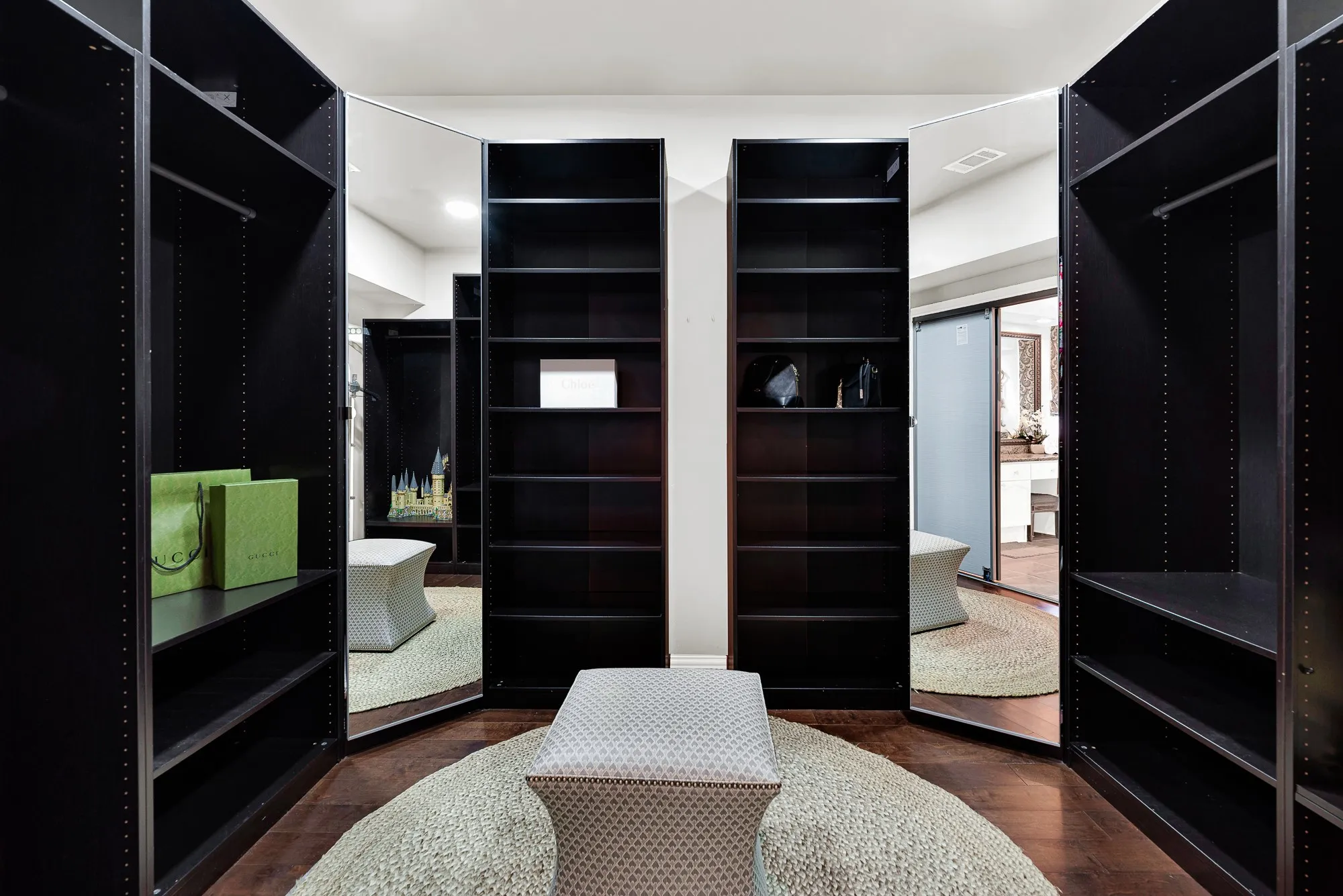 Floor-to-ceiling dark wood shelving surrounds full-length built-in mirrors in a custom private dressing layout. Easily pick out your favorite outfit while prepping for a fun evening out with friends.