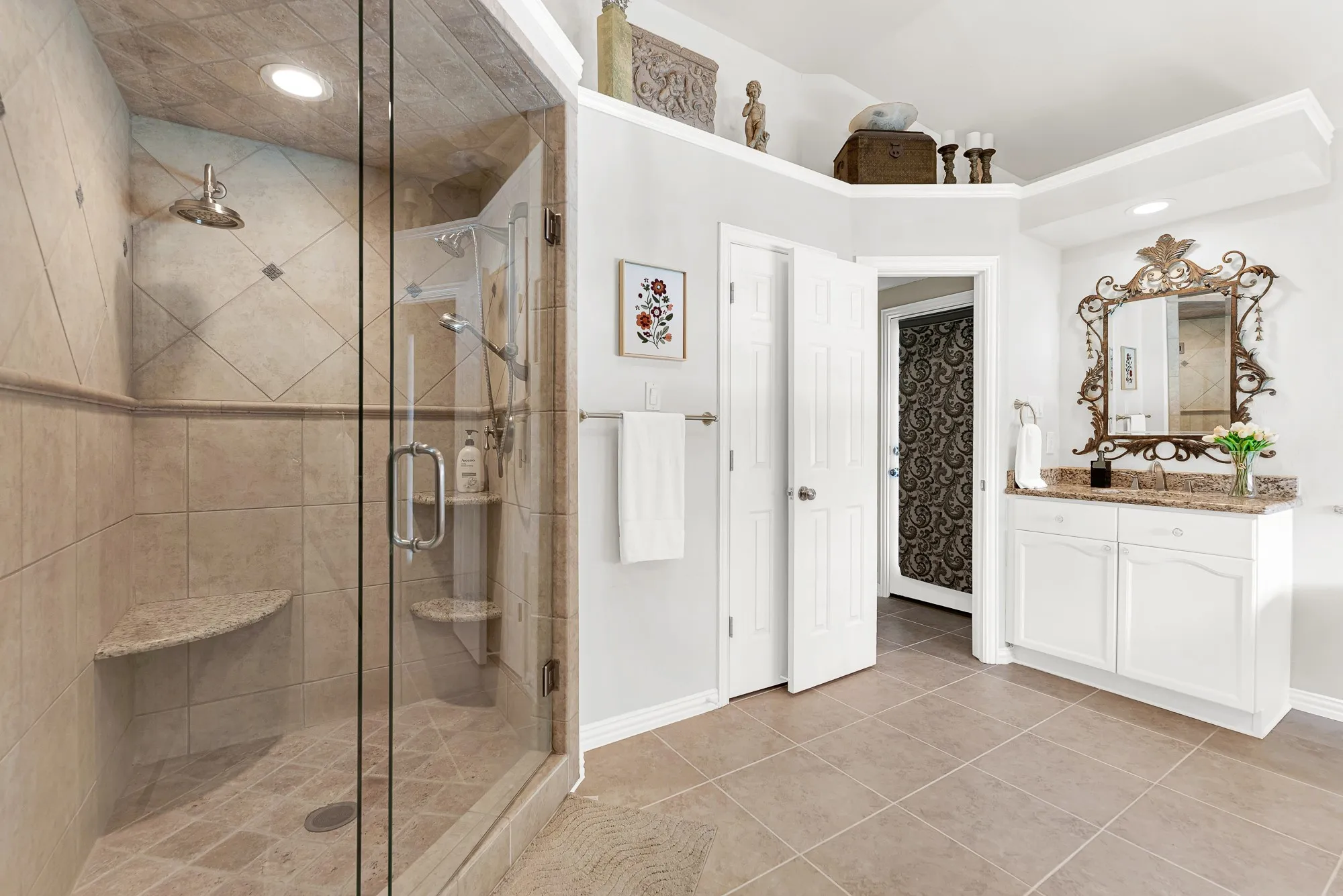 A glass-enclosed walk-in shower features seamless floor-to-ceiling travertine tile work and a built-in corner bench. Step into a steamy hot shower to energize yourself before heading out for the day.