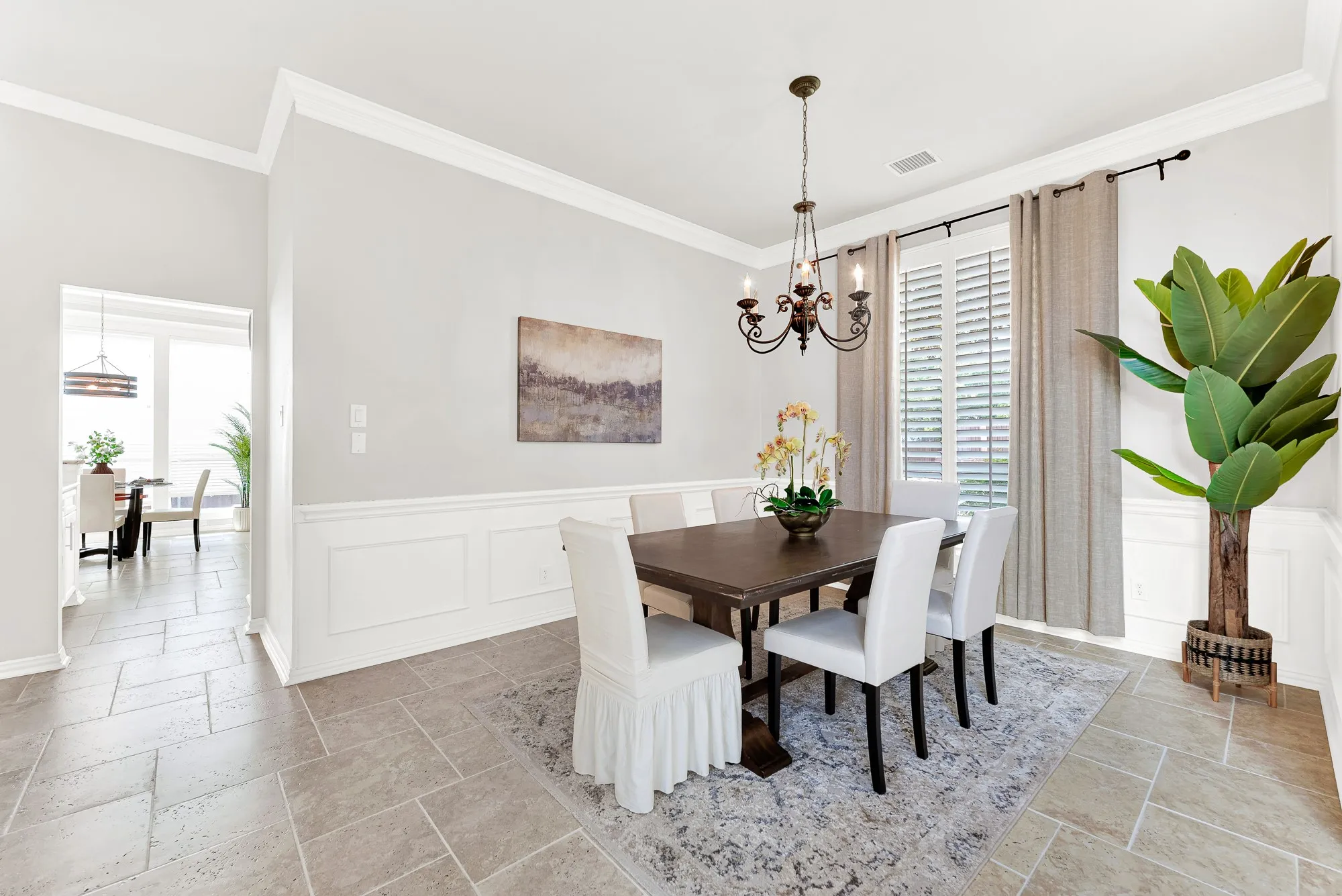 Crisp wainscoting adds refined texture around soft neutral walls illuminated by shuttered window sunlight. Gather around the table for memorable weekend family dinners filled with lively conversation.