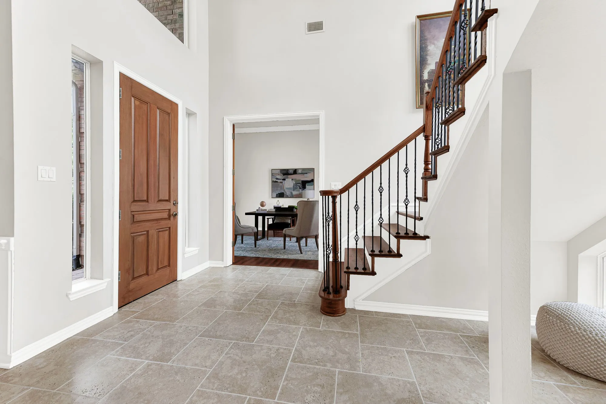 A soaring two-story ceiling and open wooden staircase frame the front doorway with clean neutral tile below. Step inside after work, drop your keys, and instantly feel the welcoming calm of home.