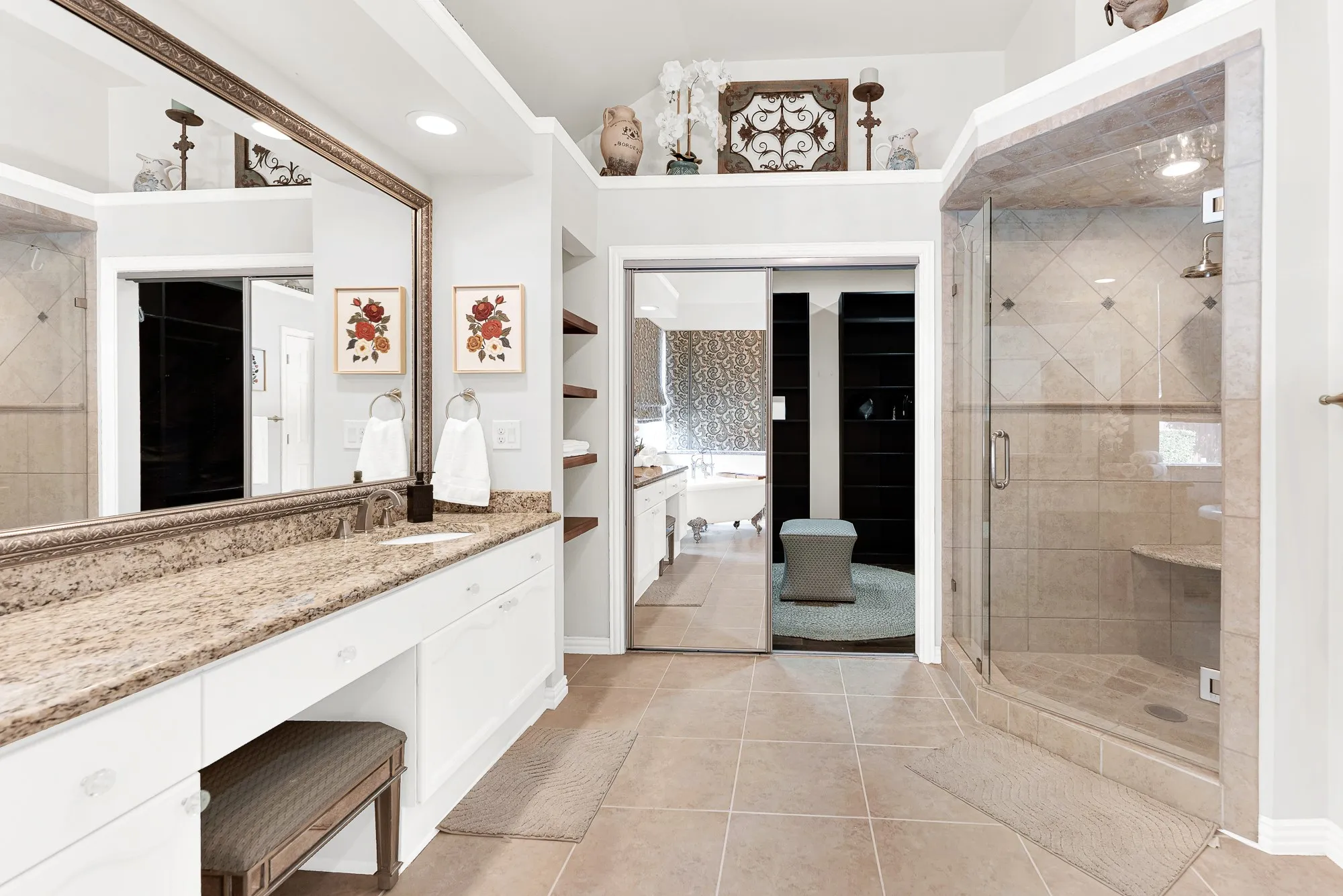 An expansive vanity topped with polished granite runs alongside open storage cubbies and mirrored sliding doors. Getting ready side-by-side during busy morning routines feels effortless and completely stress-free
