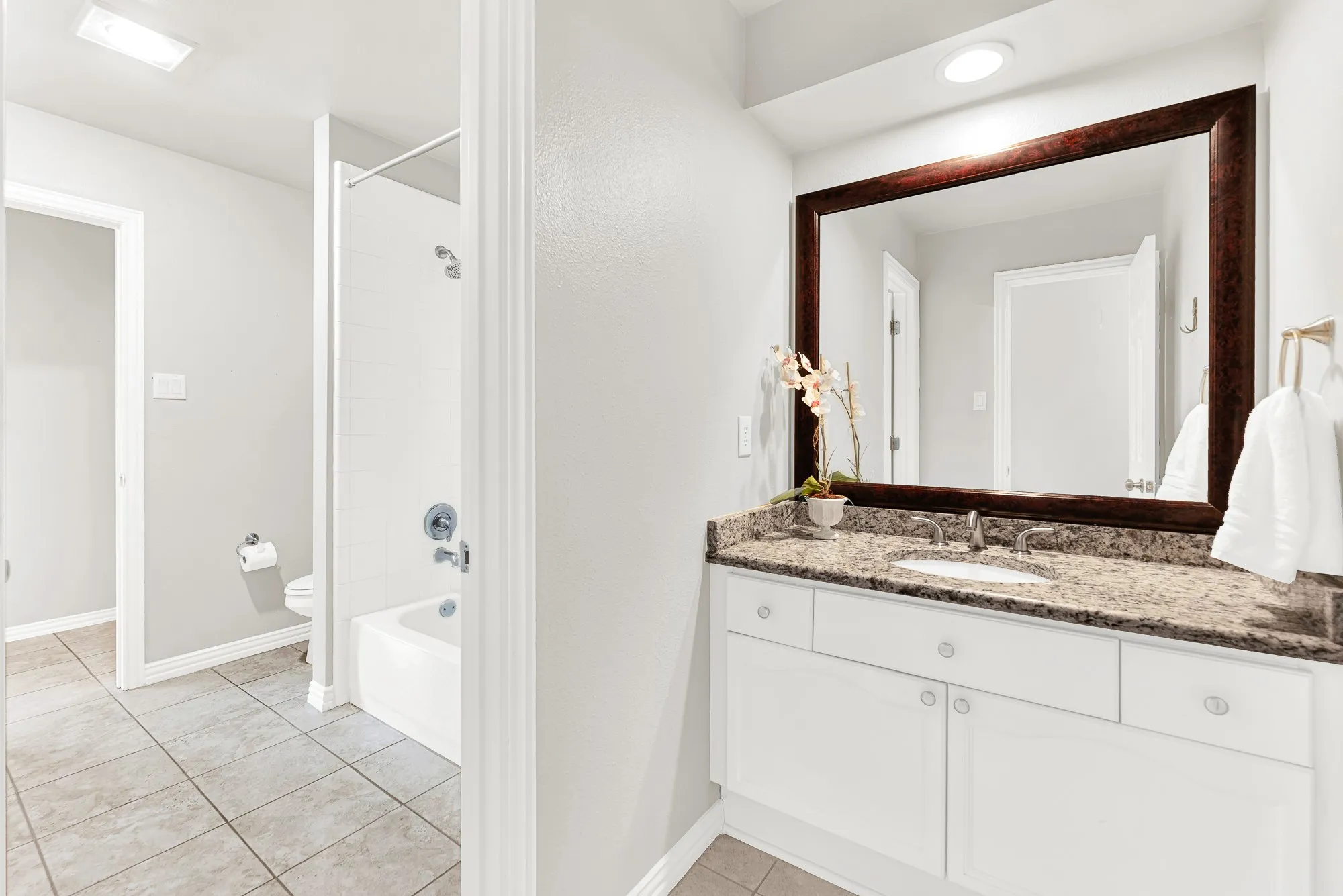 A dark wood framed mirror reflects natural vanity light above a speckled granite counter and separate wet area. Kids can prepare for school simultaneously without stepping on each other's toes during early mornings