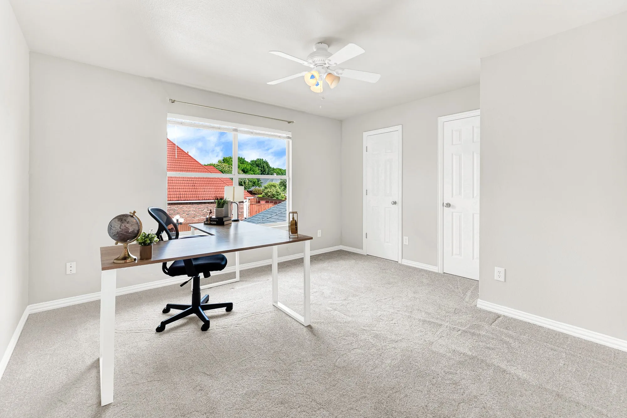 A bright square window frames rooftop views while filling soft carpeted flooring with morning light in this guest bedroom or home office. You can focus comfortably on remote work projects in a quiet retreat away from main household bustle