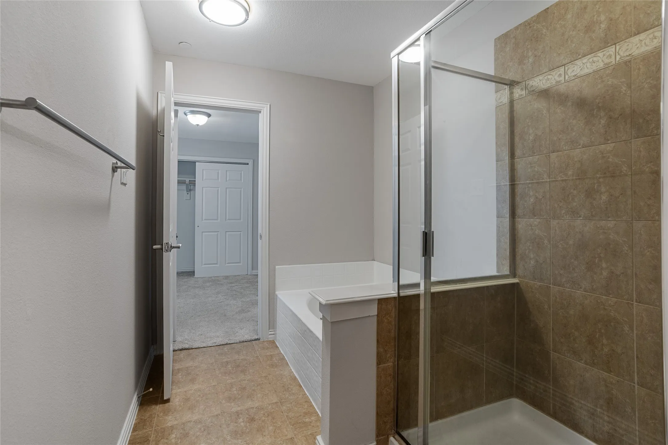 Glass-enclosed shower with brown tile surround, built-in soaking tub, wood-finish flooring, and flush mount lighting