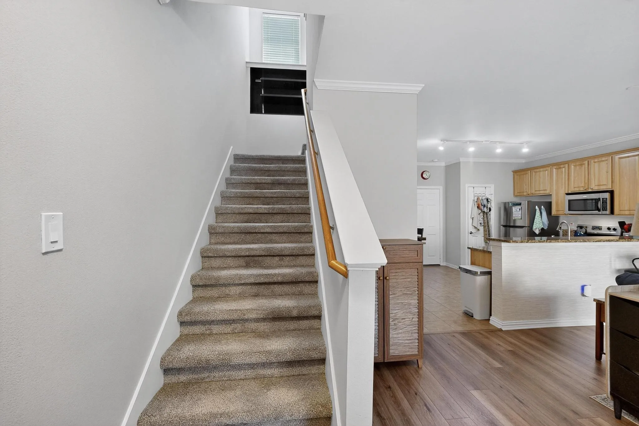 Carpeting on staircase with a wood handrail, crown molding, wood-finish flooring, and a kitchen featuring wood cabinetry and stainless steel appliances