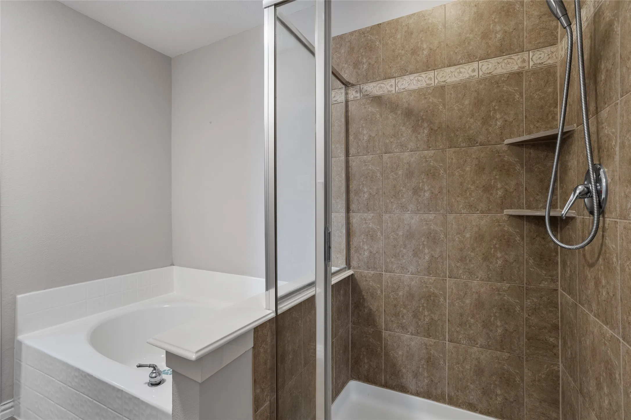 Modern bathroom featuring a ceramic soaking tub with chrome fixtures, a frameless glass-enclosed shower with tile surround and integrated shelving, dual showerheads, and neutral tile flooring throughout