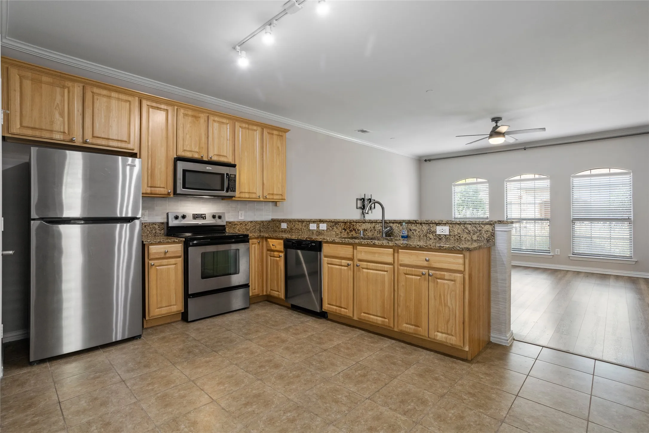 Kitchen featuring stainless steel appliances, wood cabinetry, stone countertops, and tile flooring