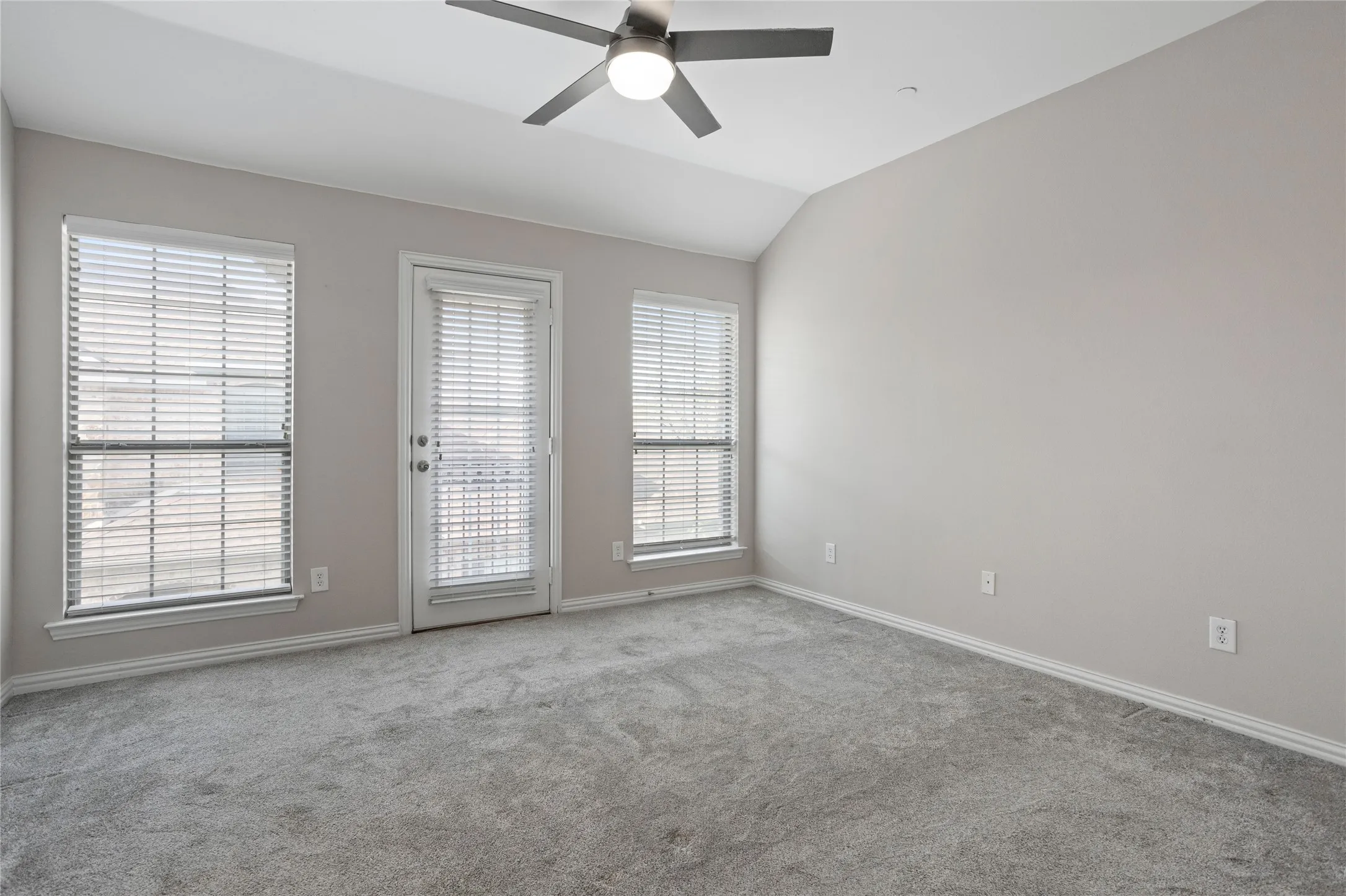 Vaulted ceiling, ceiling fan with integrated lighting, door with integrated blinds, two windows with integrated blinds, and plush carpeting