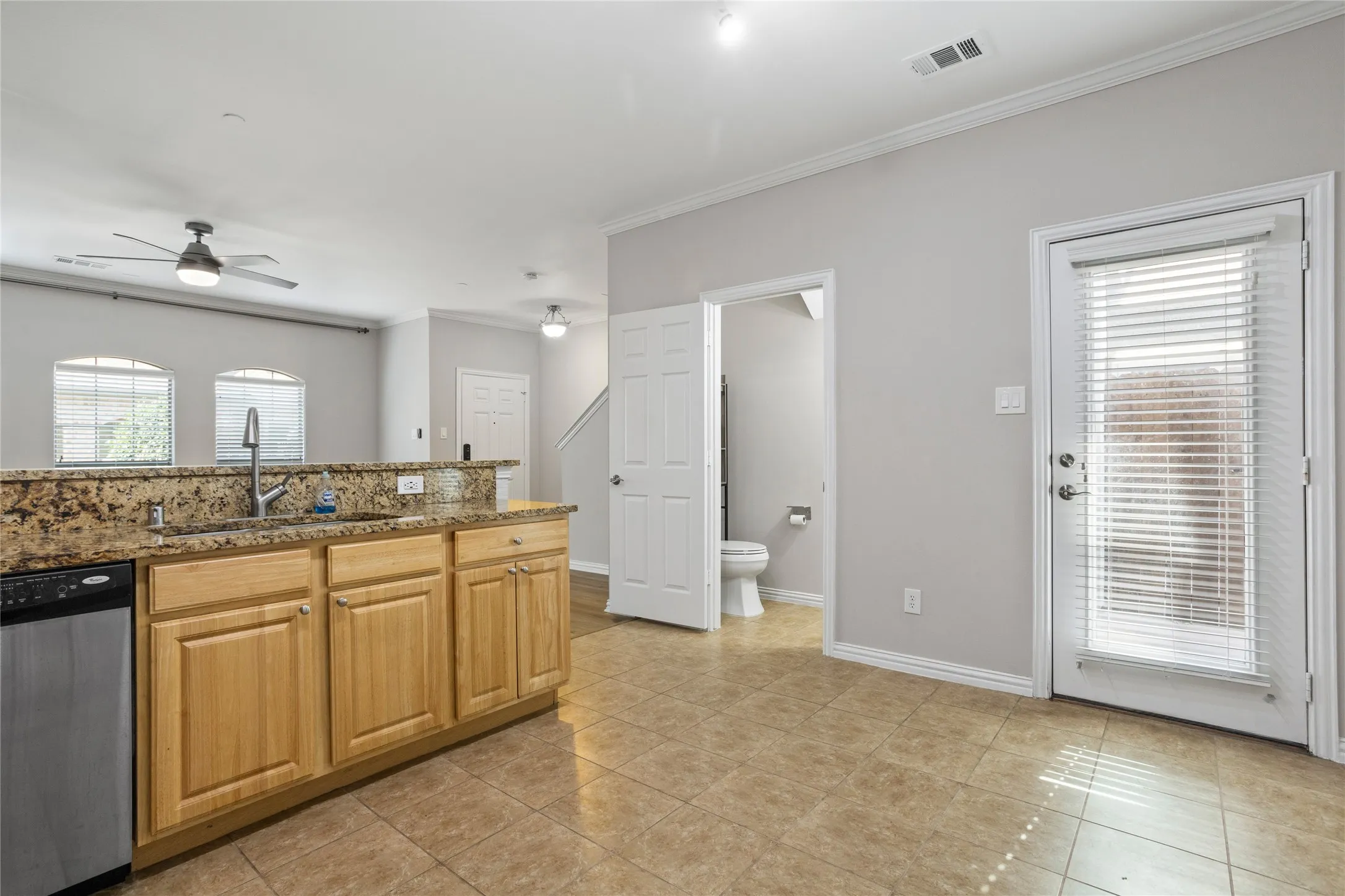 Kitchen with wood cabinetry, granite countertops, stainless steel dishwasher, and tile flooring