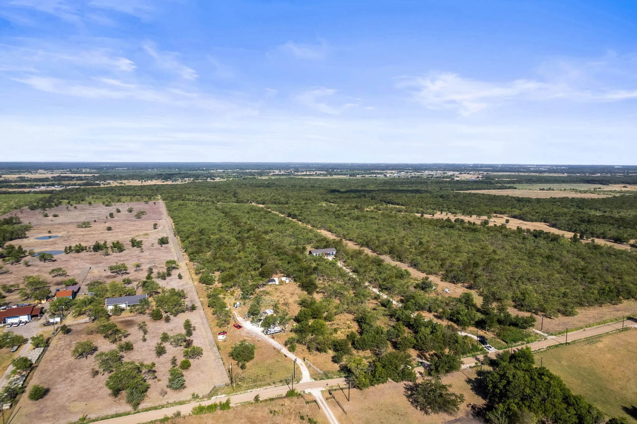 Expansive acreage with diverse terrain, featuring wooded sections, open fields, and established structures