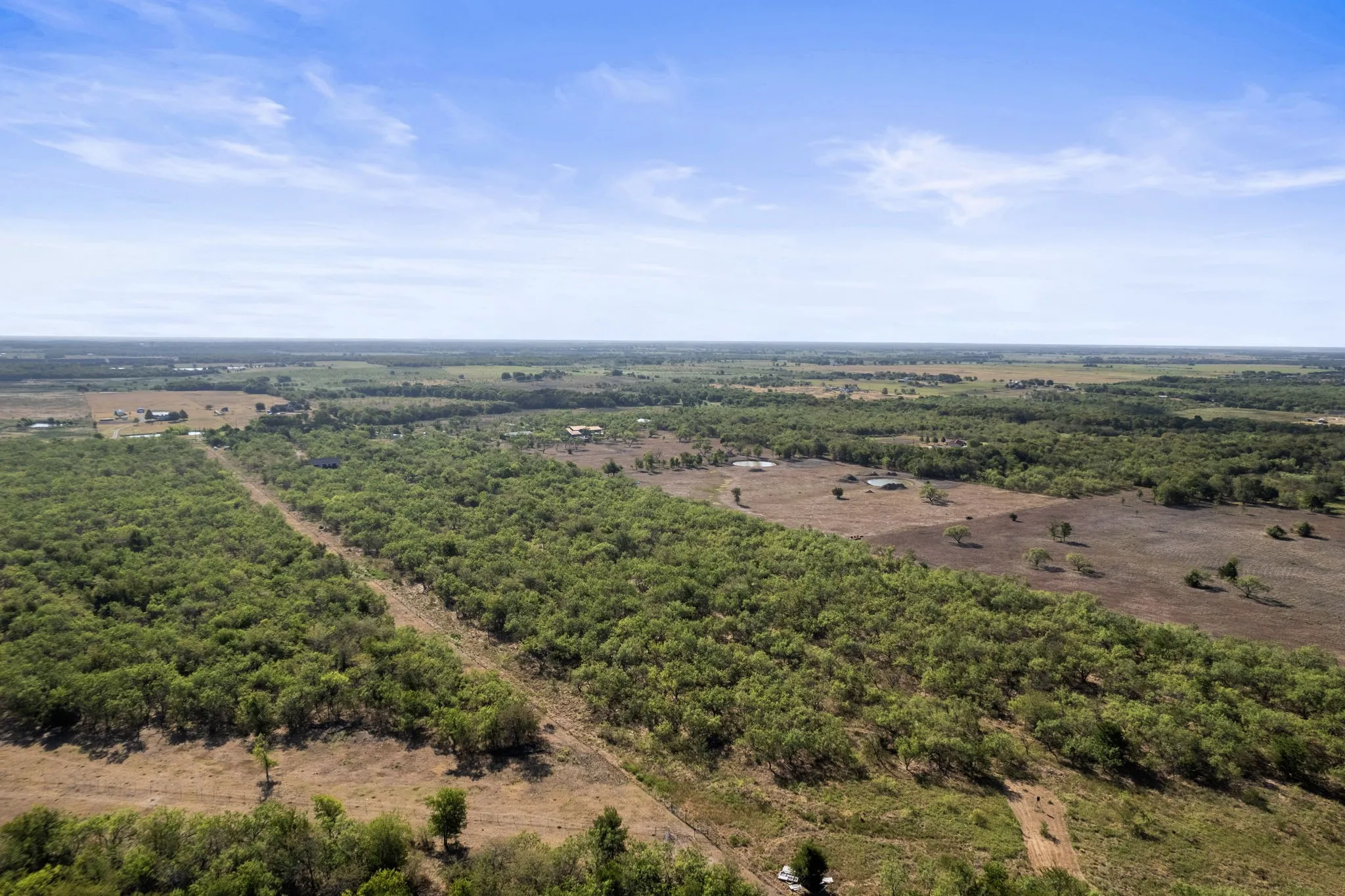 Expansive land featuring mature tree lines and clearings, with distant structures visible