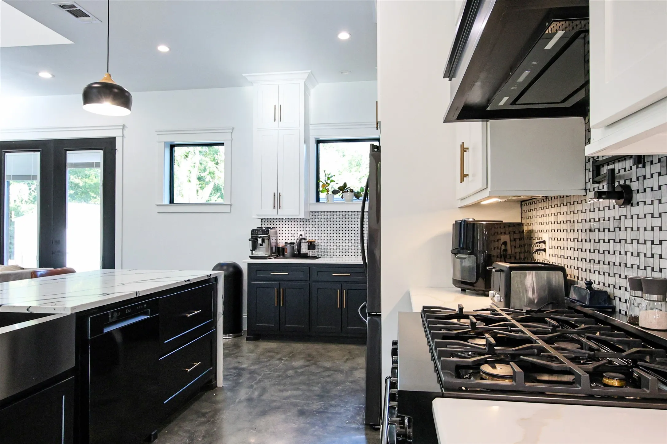 Contemporary kitchen featuring a gas range, dual-tone cabinetry, patterned backsplash, a kitchen island with an undermount sink, and recessed lighting