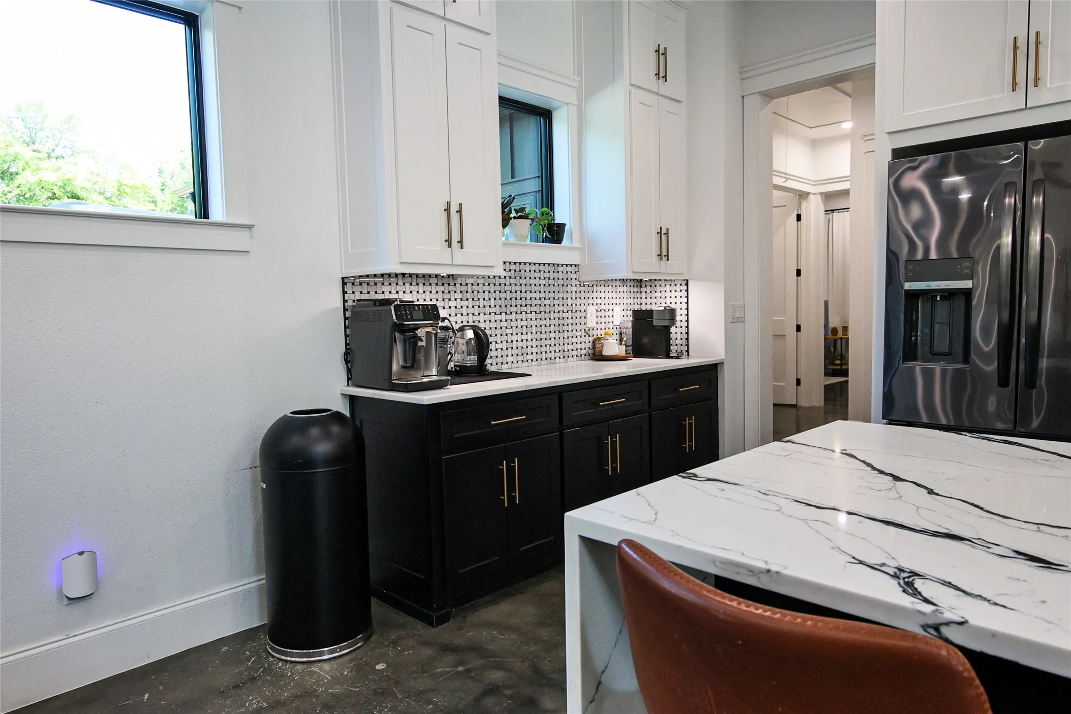 White upper cabinetry, black lower cabinetry, patterned tile backsplash, light-toned countertop, and a built-in stainless steel refrigerator
