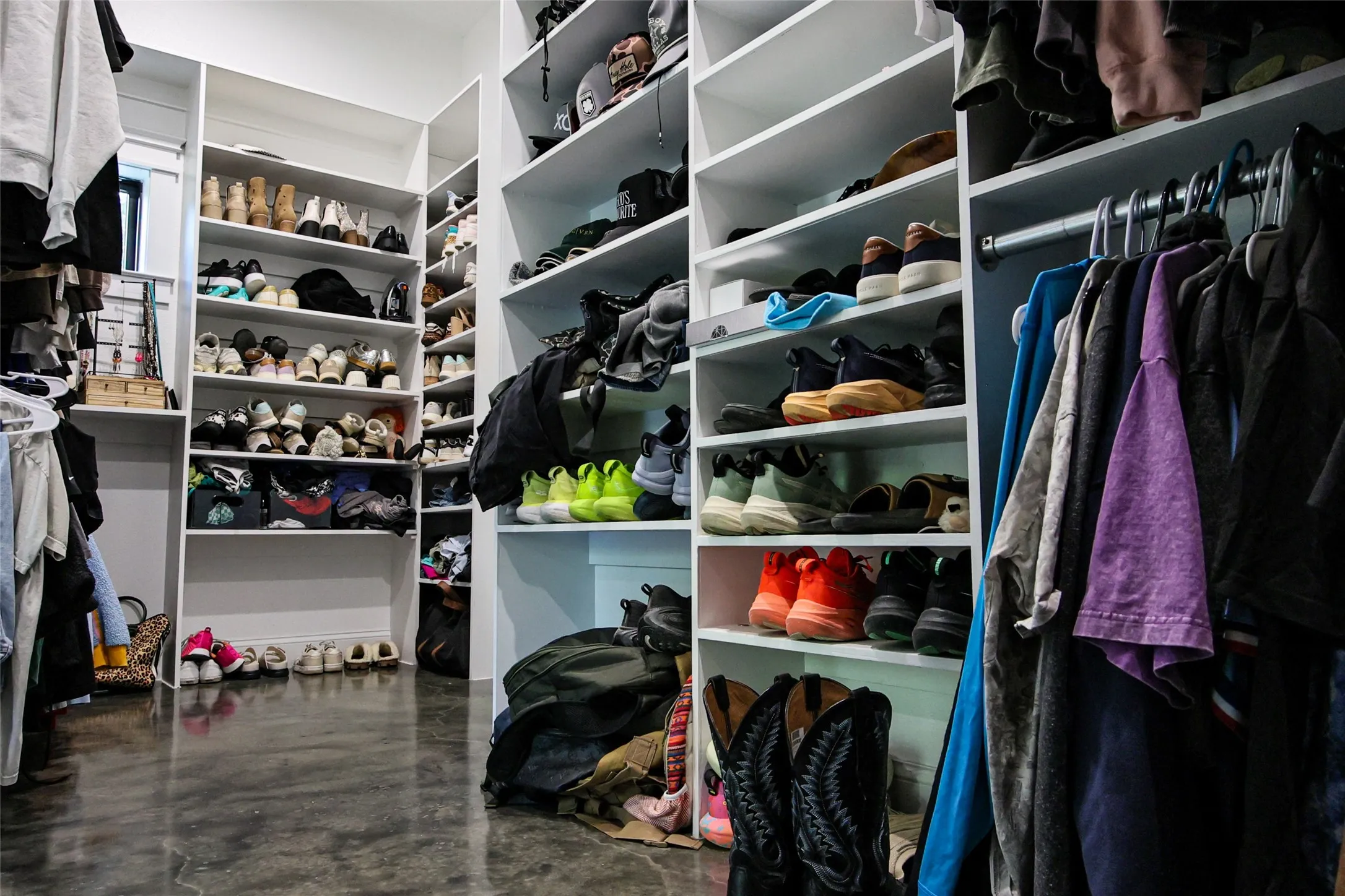 Custom closet organization system with extensive shelving, multiple hanging rods, and a polished concrete floor