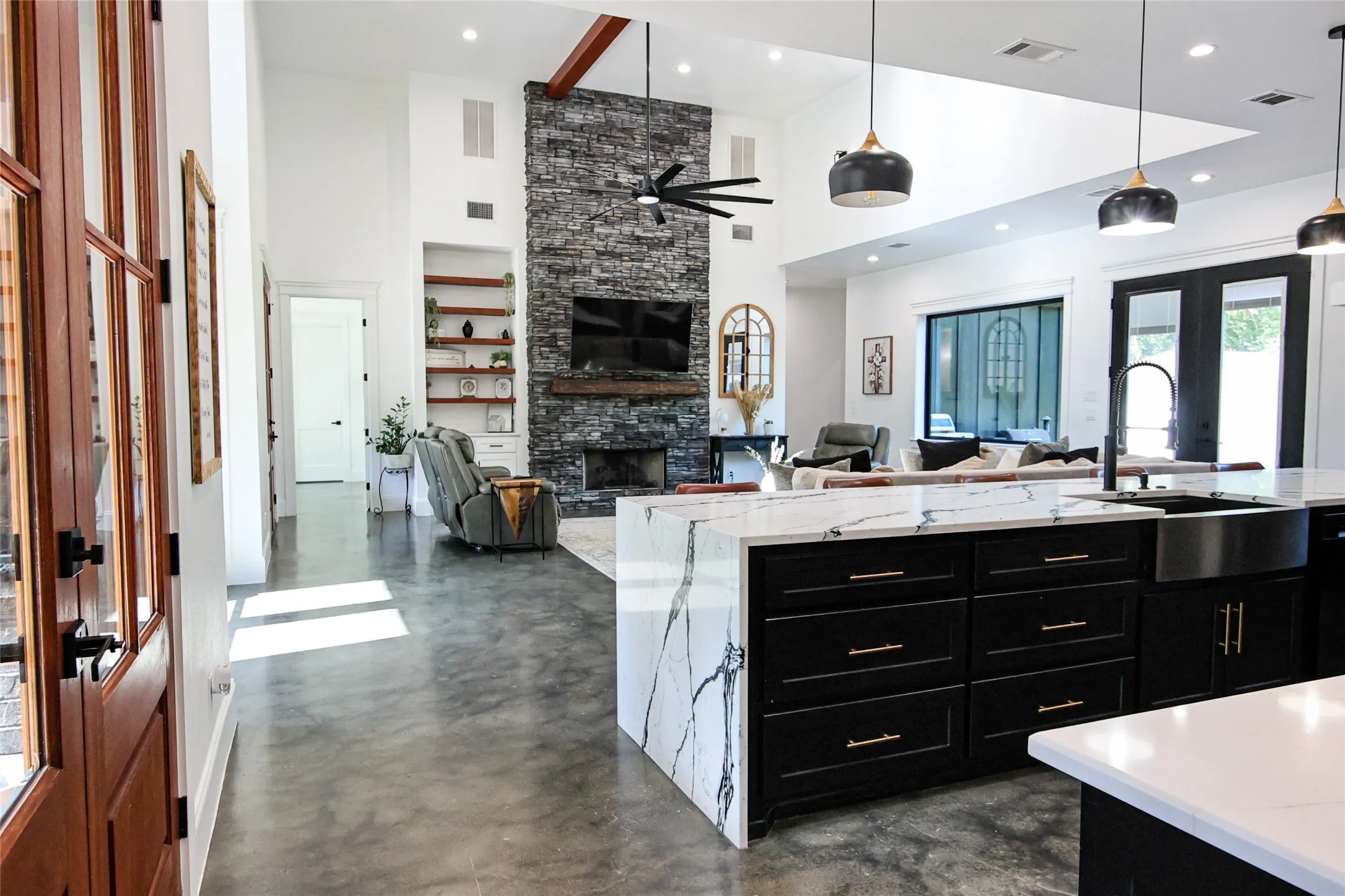 Spacious open-concept interior featuring high ceilings, a floor-to-ceiling stone fireplace, and polished concrete flooring