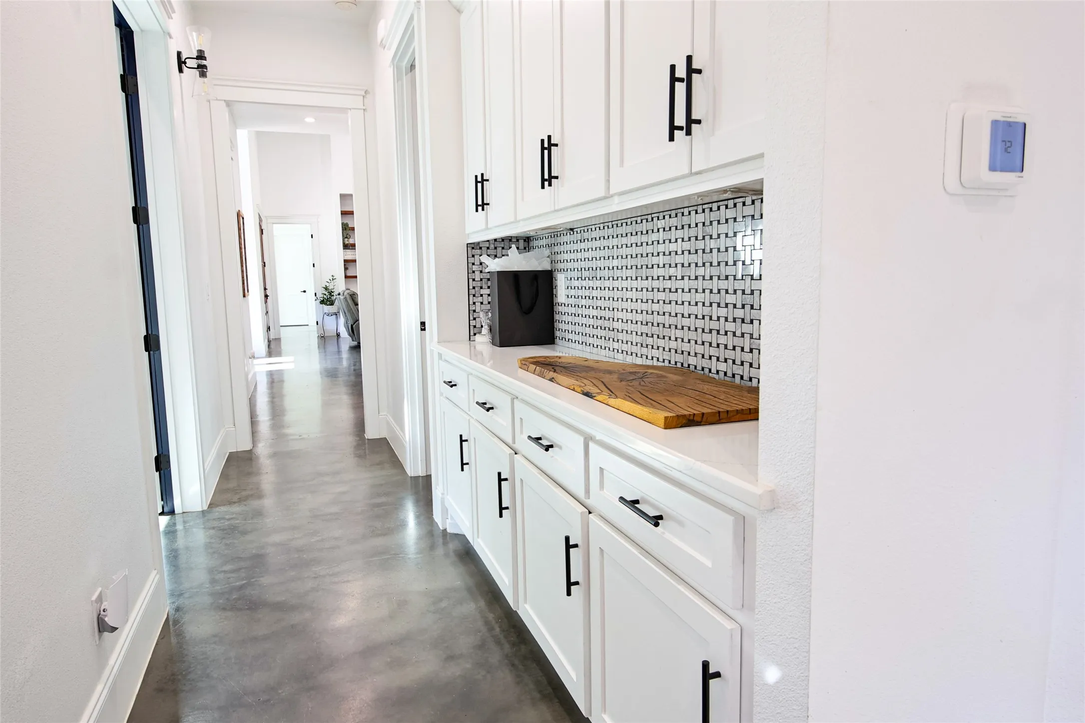 White cabinetry with matte black hardware, white countertop, mosaic tile backsplash, and concrete flooring