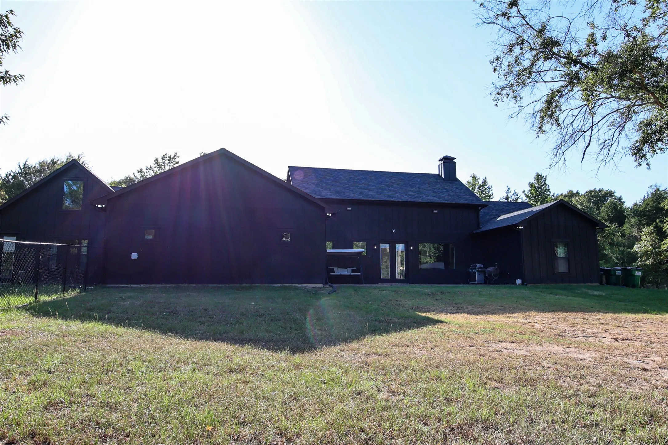 Expansive exterior featuring dark siding, multiple pitched rooflines, a prominent chimney, and a chain-link fence