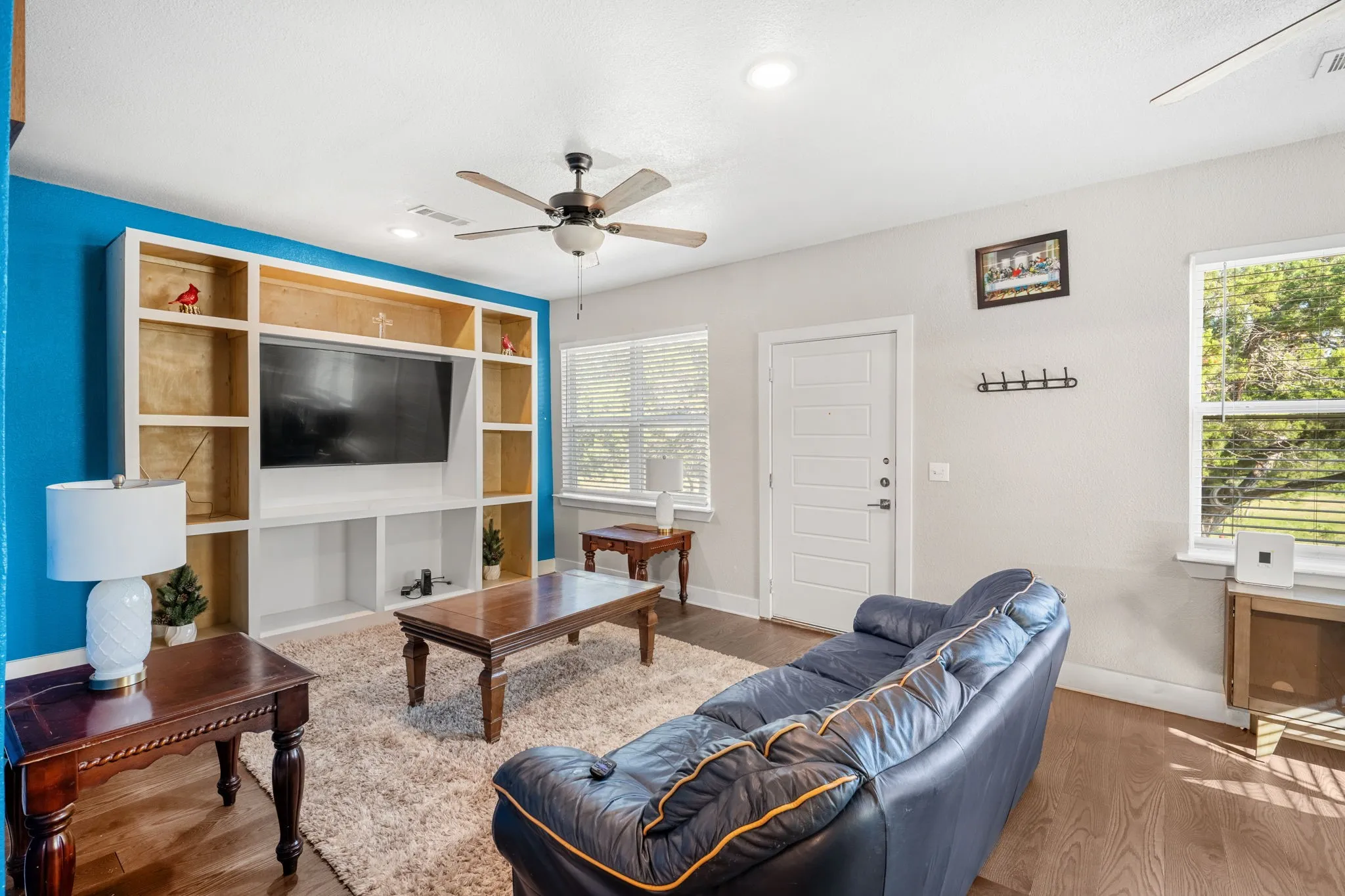 Wood-finish flooring, built-in entertainment center with shelving, white paneled door, recessed lighting, and a ceiling fan with integrated light
