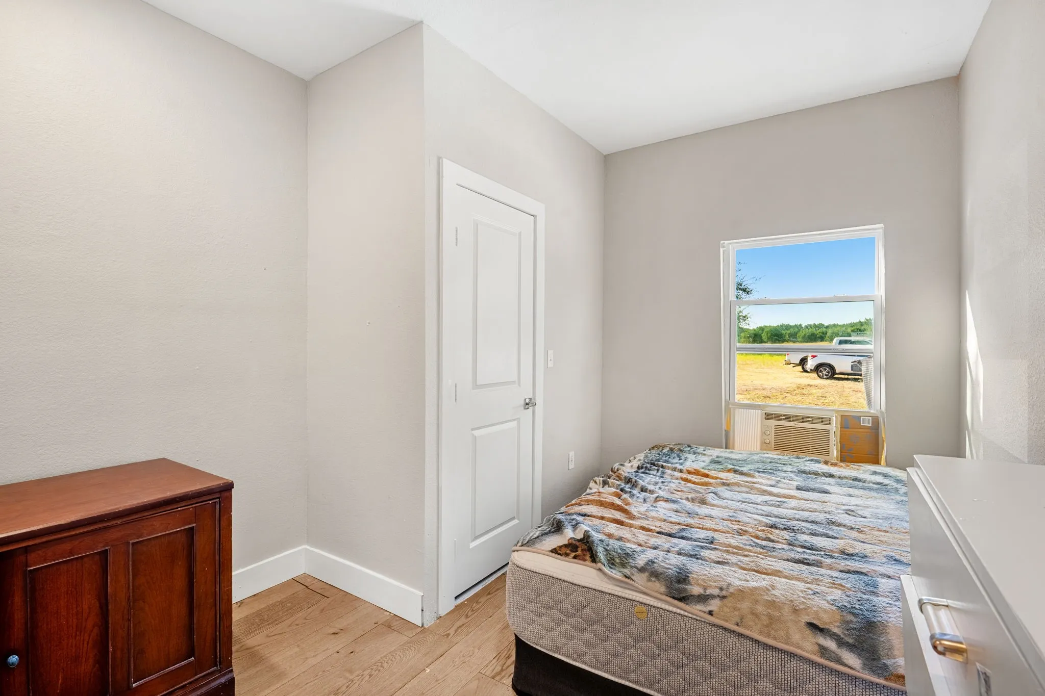 Wood-finish flooring with white trim, a single-pane window, and a white interior door