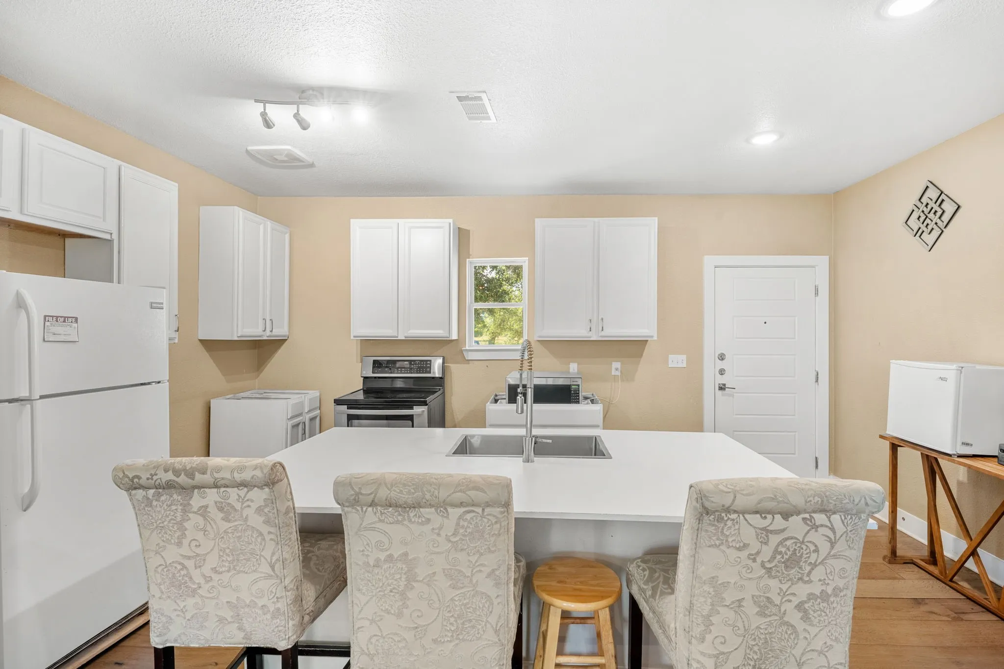 Kitchen featuring a white appliance package, white cabinetry, a center island with an undermount sink, and recessed lighting