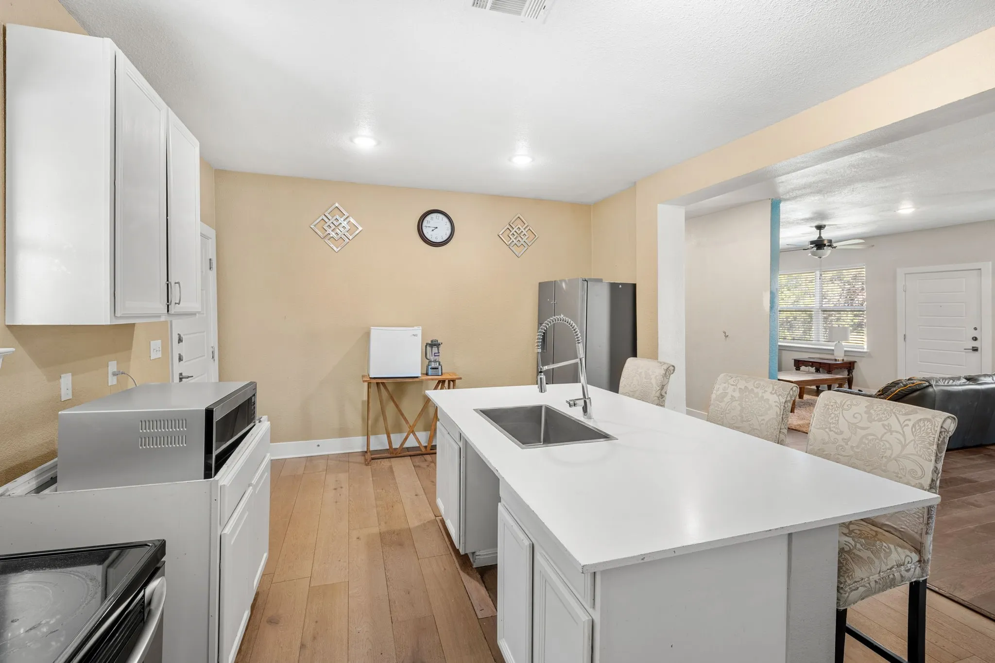 Kitchen featuring a large center island with integrated sink, white cabinetry, and wood-finish flooring