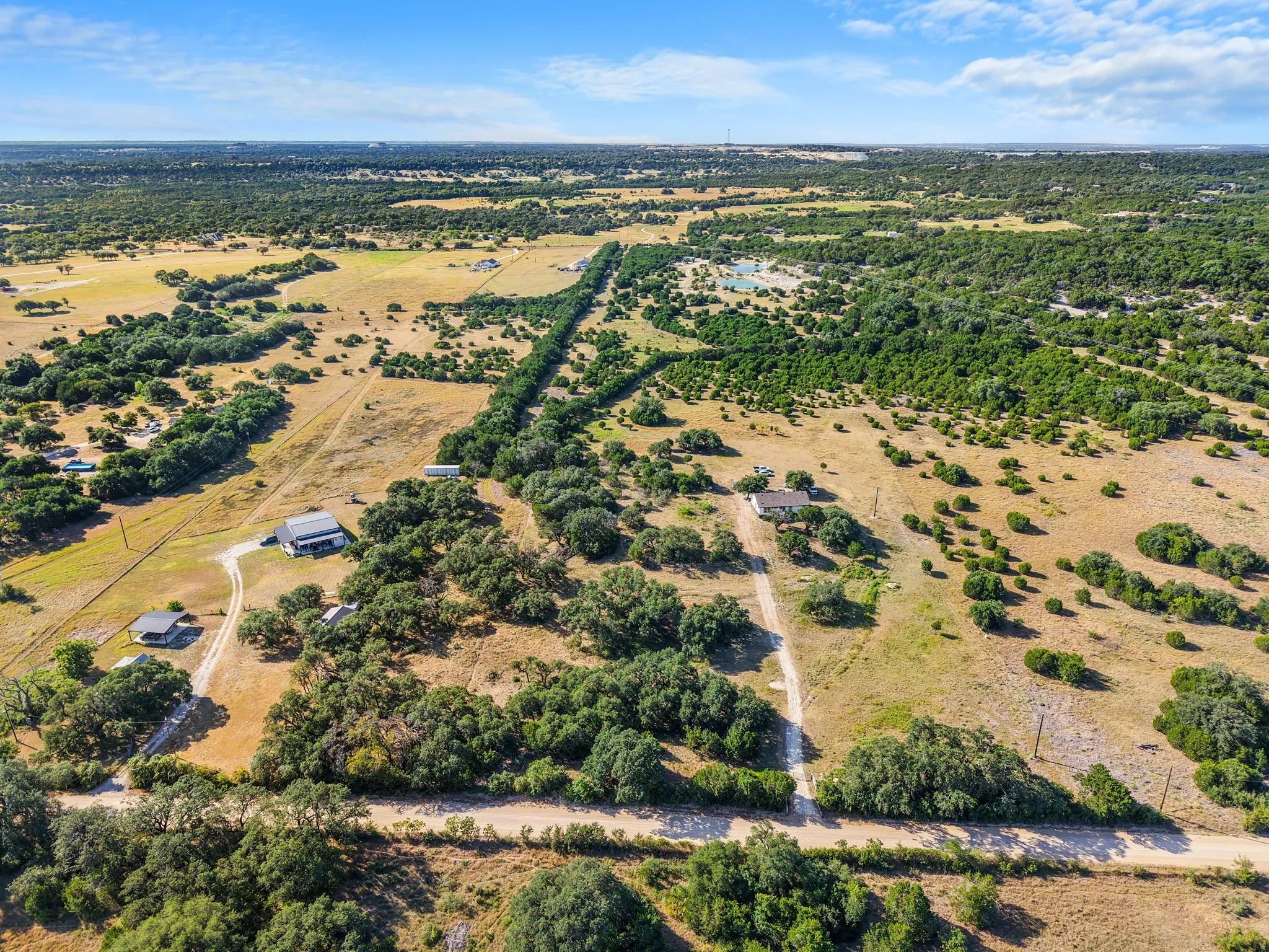 Expansive rural landscape featuring scattered trees, residential structures, and natural terrain