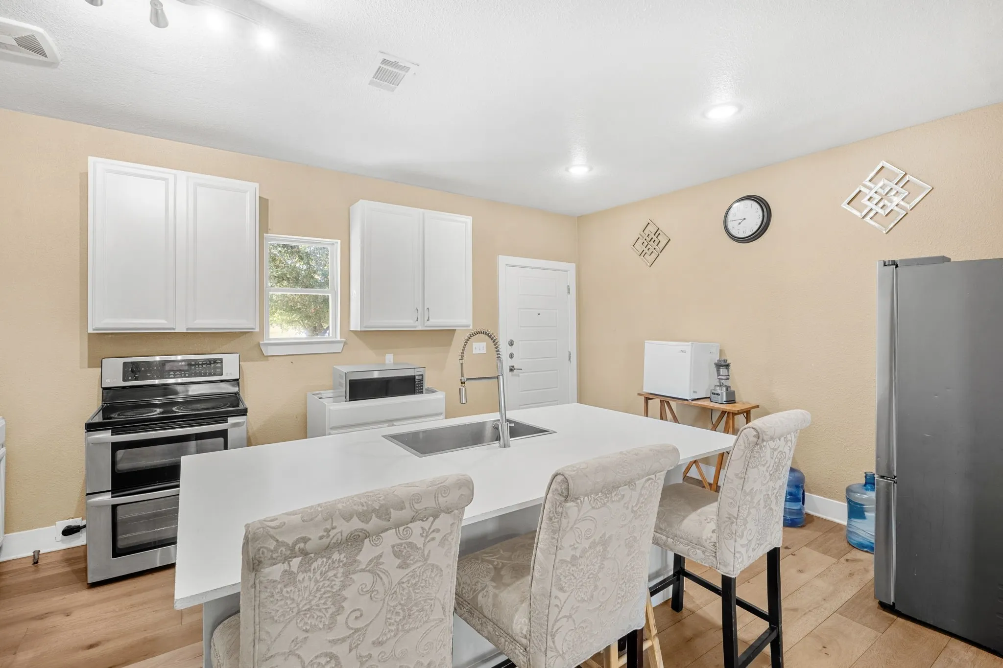 Modern kitchen featuring a central island with an integrated sink, white cabinetry, stainless steel appliances, and wood-finish flooring