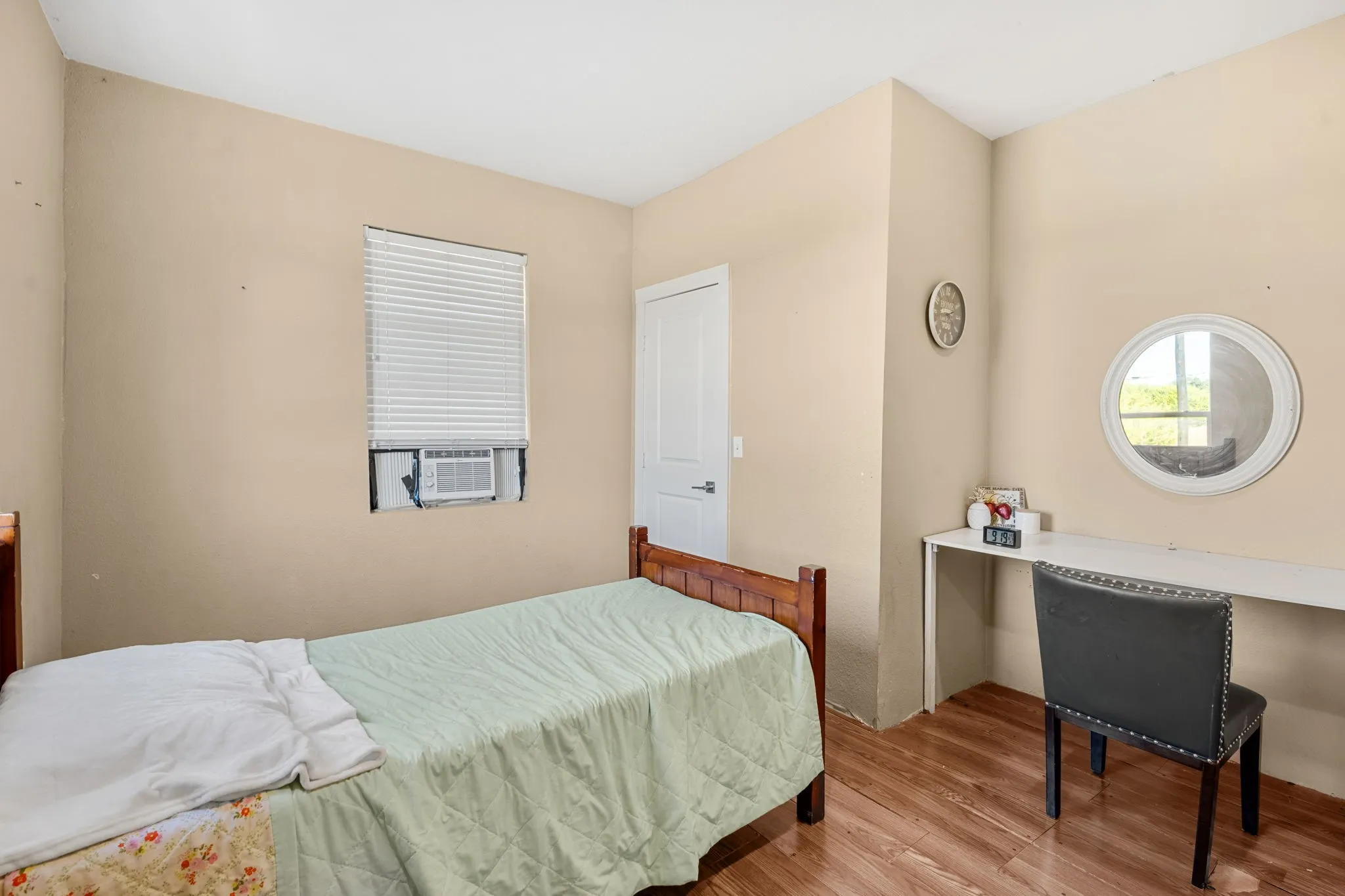Wood-finish flooring with a neutral wall color, built-in desk, and a window featuring an air conditioning unit
