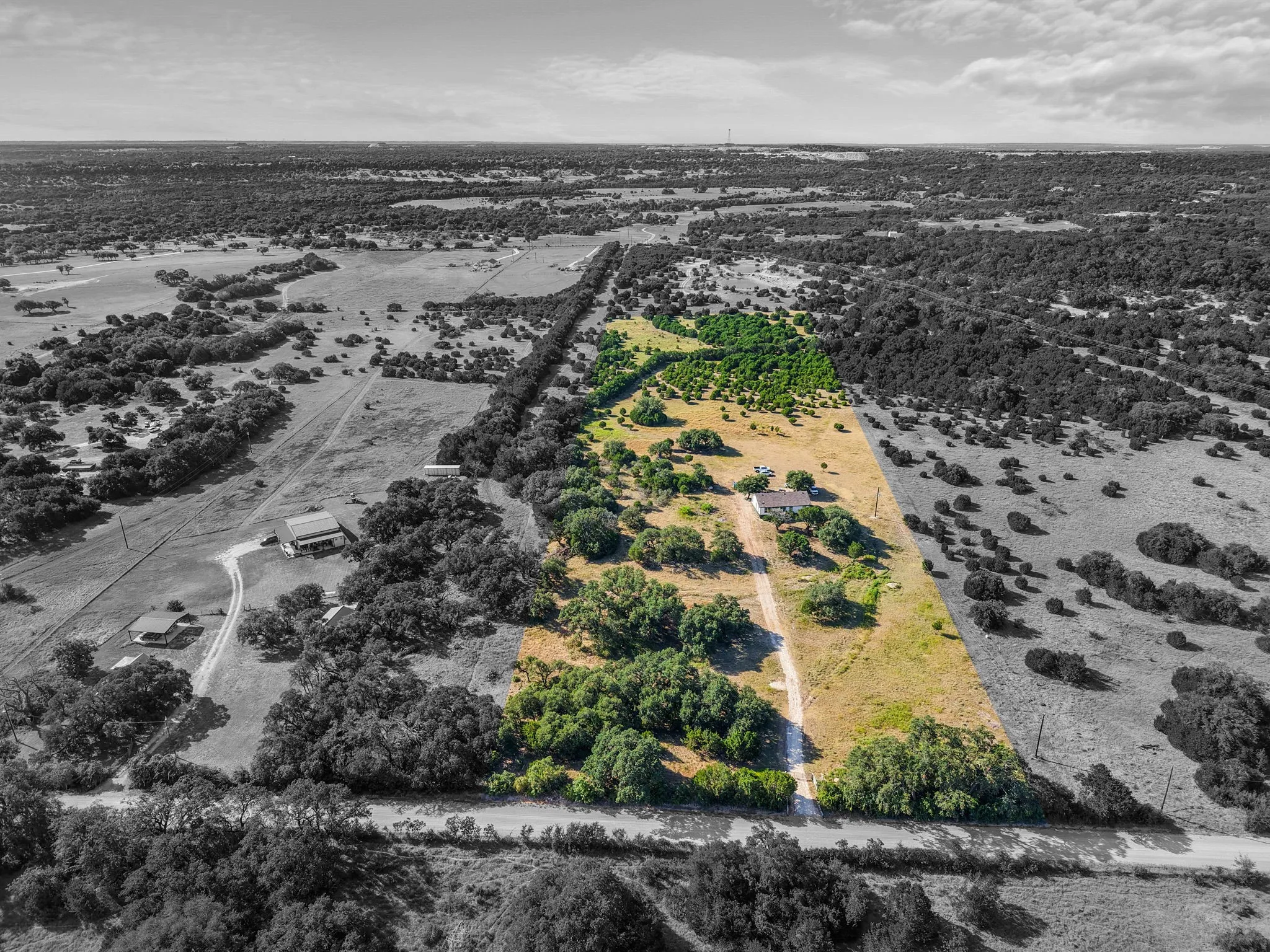 Expansive rural acreage with scattered trees and a visible residential structure