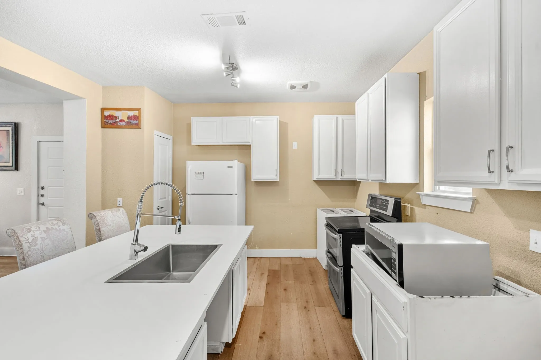 Kitchen featuring white cabinetry, wood-finish flooring, a stainless steel sink with a pull-down faucet, and a large central island