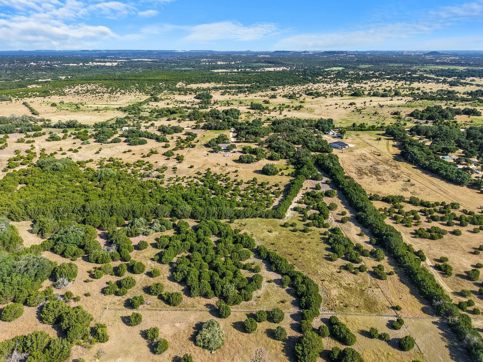 Expansive rural landscape featuring scattered trees, open fields, and distant structures